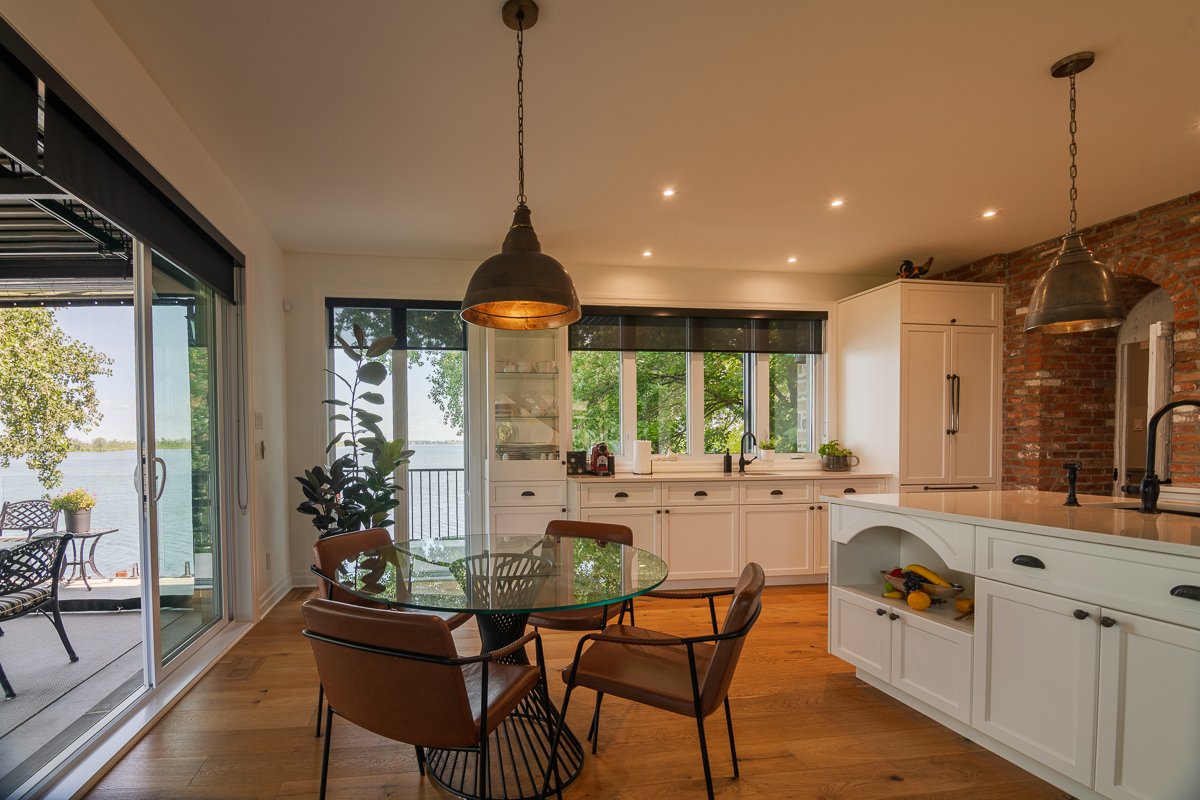 Breakfast area with a round glass table and tan leather chairs, opening through a slider to a lakeside terrace