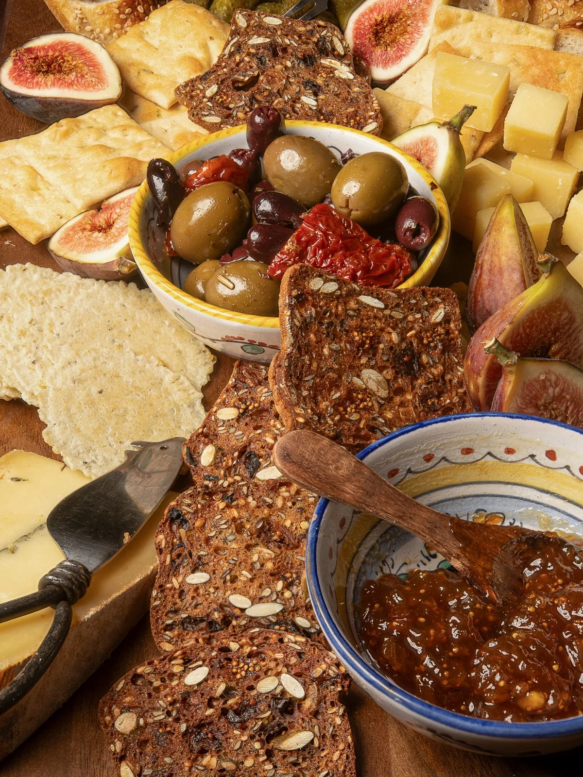 Charcuterie board with figs, olives, cheese, and seeded crackers.