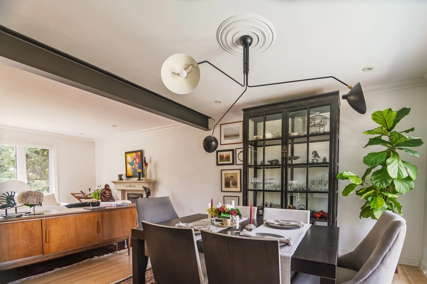 Dining room with a black glass-front cabinet holding glassware and silver, under an articulated three-arm ceiling fixture