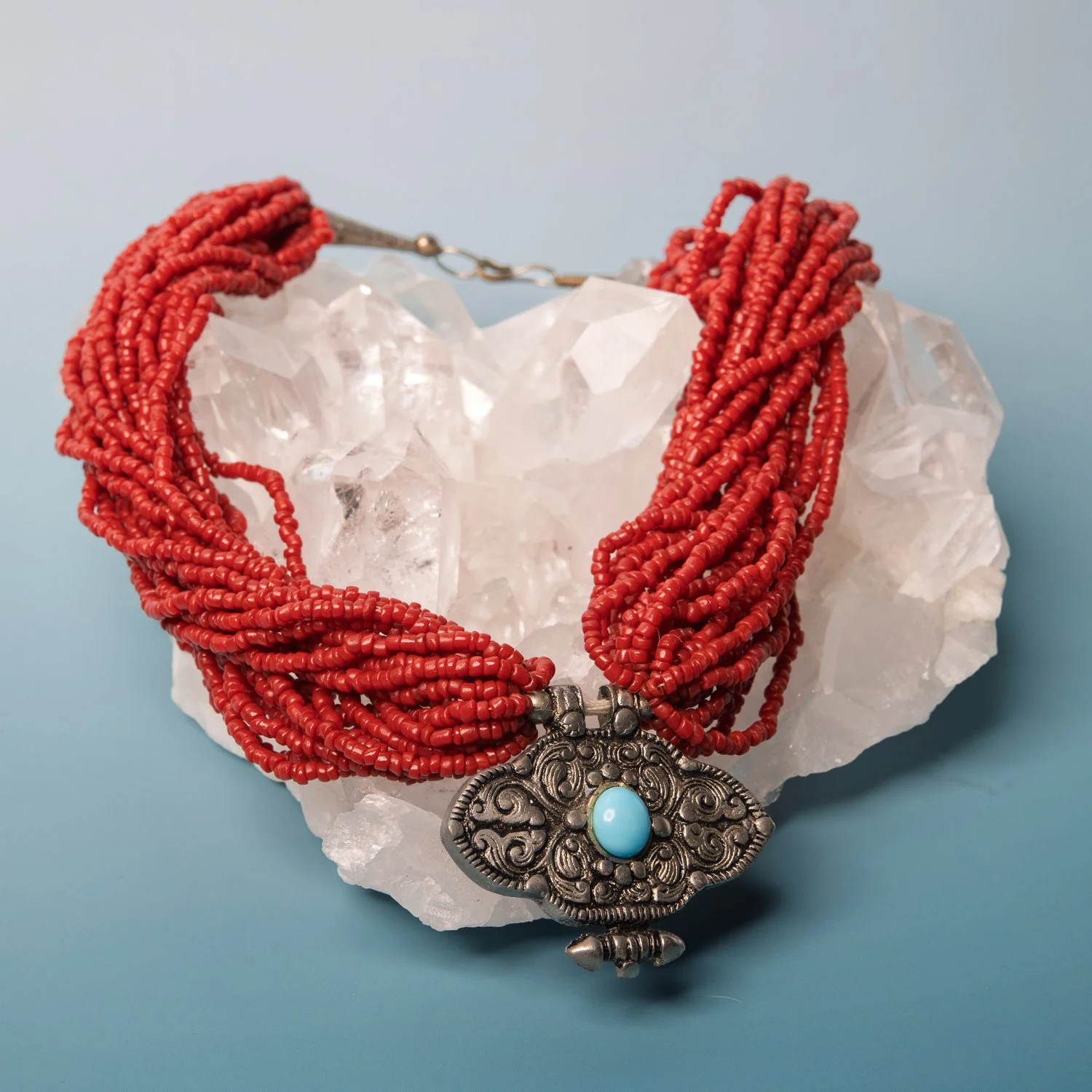 A multi-strand red coral necklace draped over a raw quartz crystal.