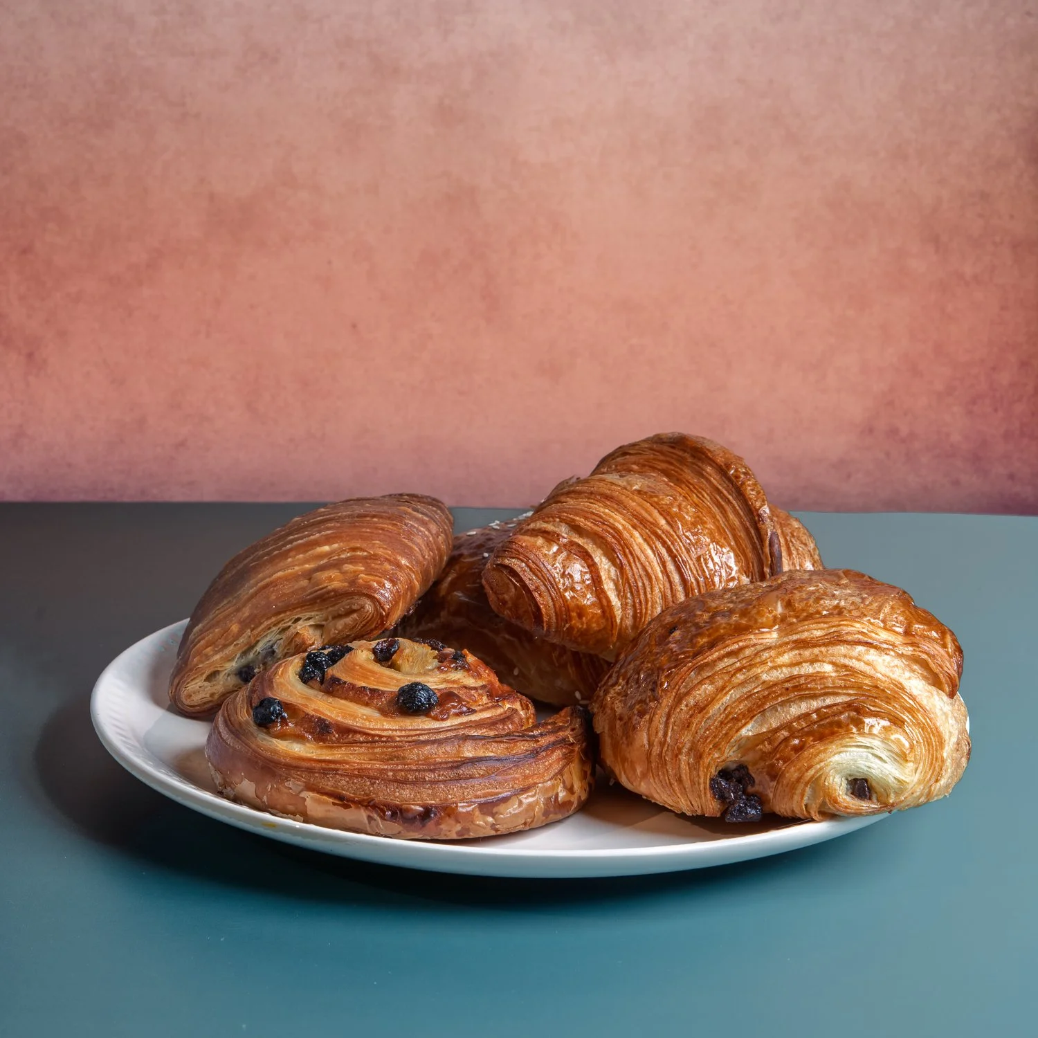 Croissants and pain au chocolat on a white plate.