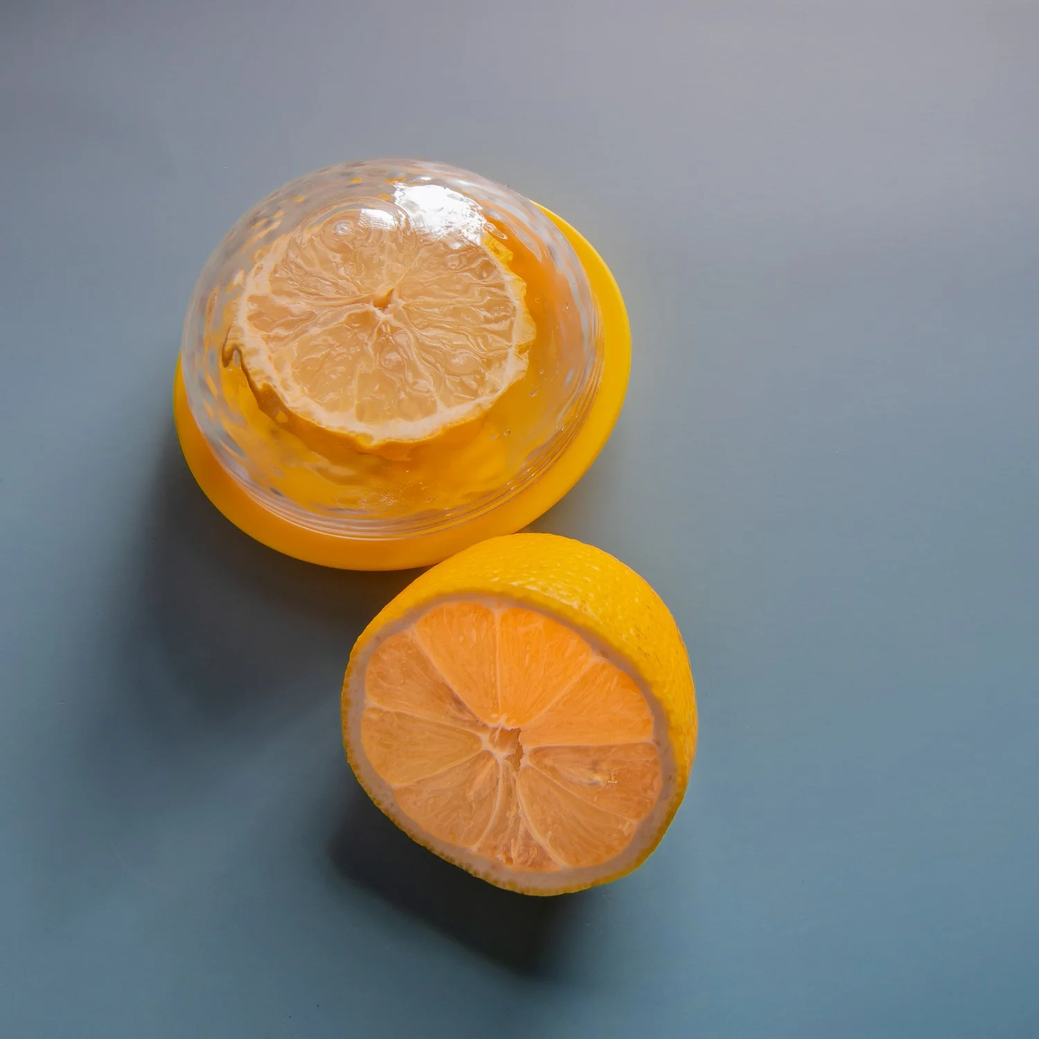 A yellow plastic lemon keeper with a clear dome lid, beside a cut lemon half.