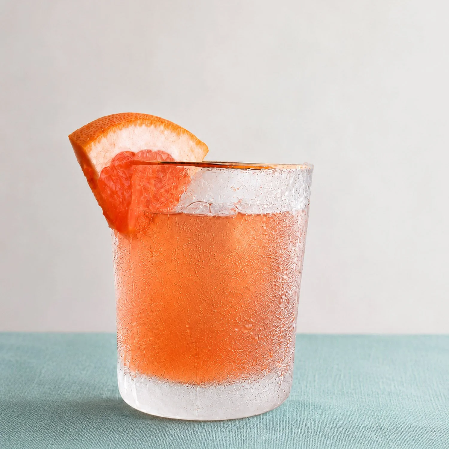 Grapefruit cocktail in a frosted glass on a blue surface.
