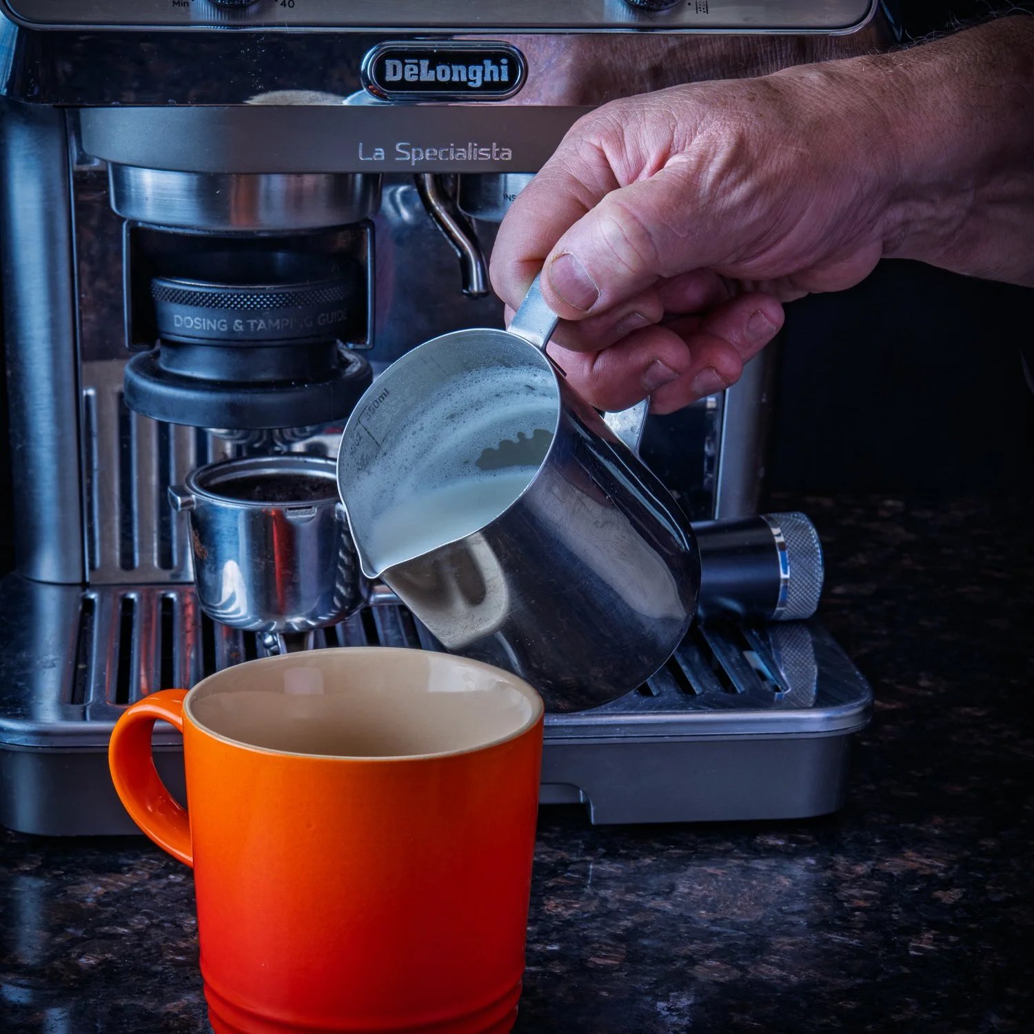 Milk being poured into a cup from an espresso machine's pitcher.