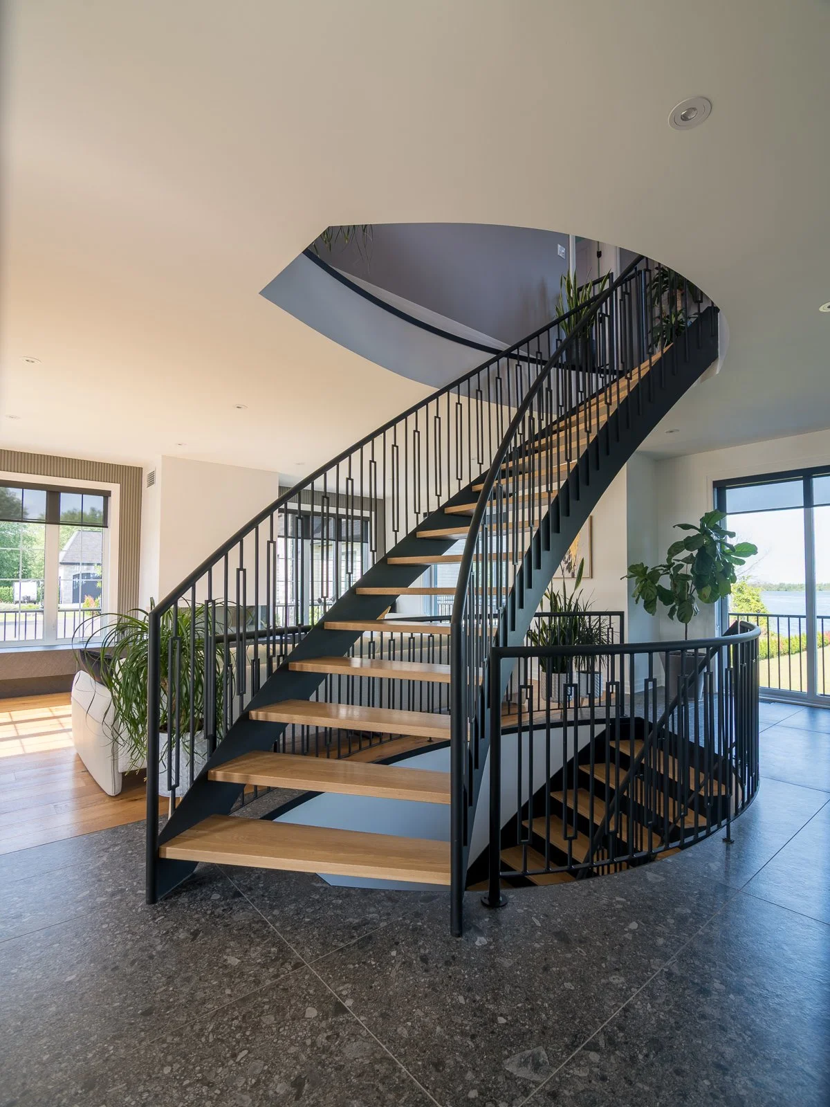 Interiors Curved open-tread staircase in black steel and oak rising through a double-height entry hall above a terrazzo floor