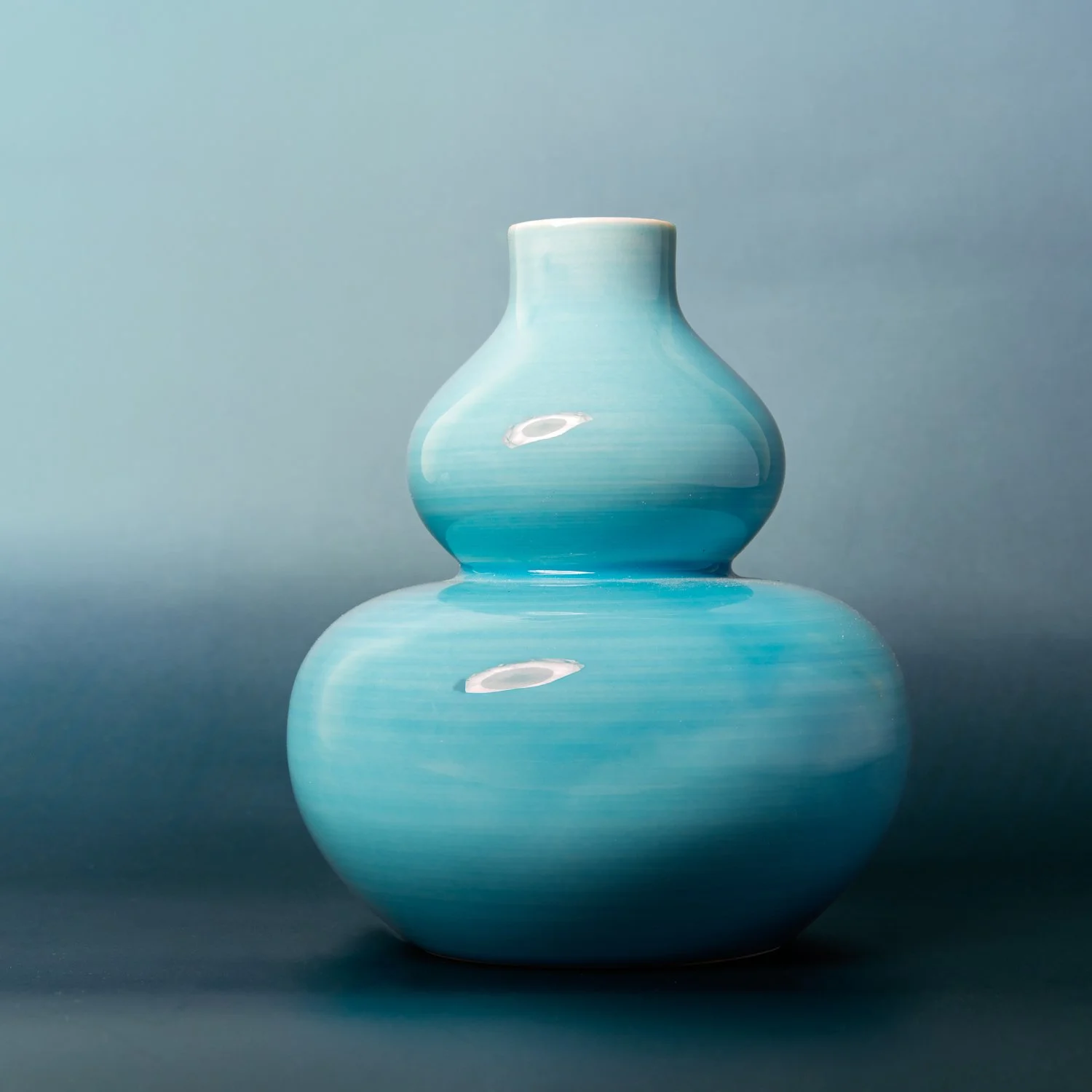 A turquoise gourd-shaped ceramic vase against a blue backdrop.