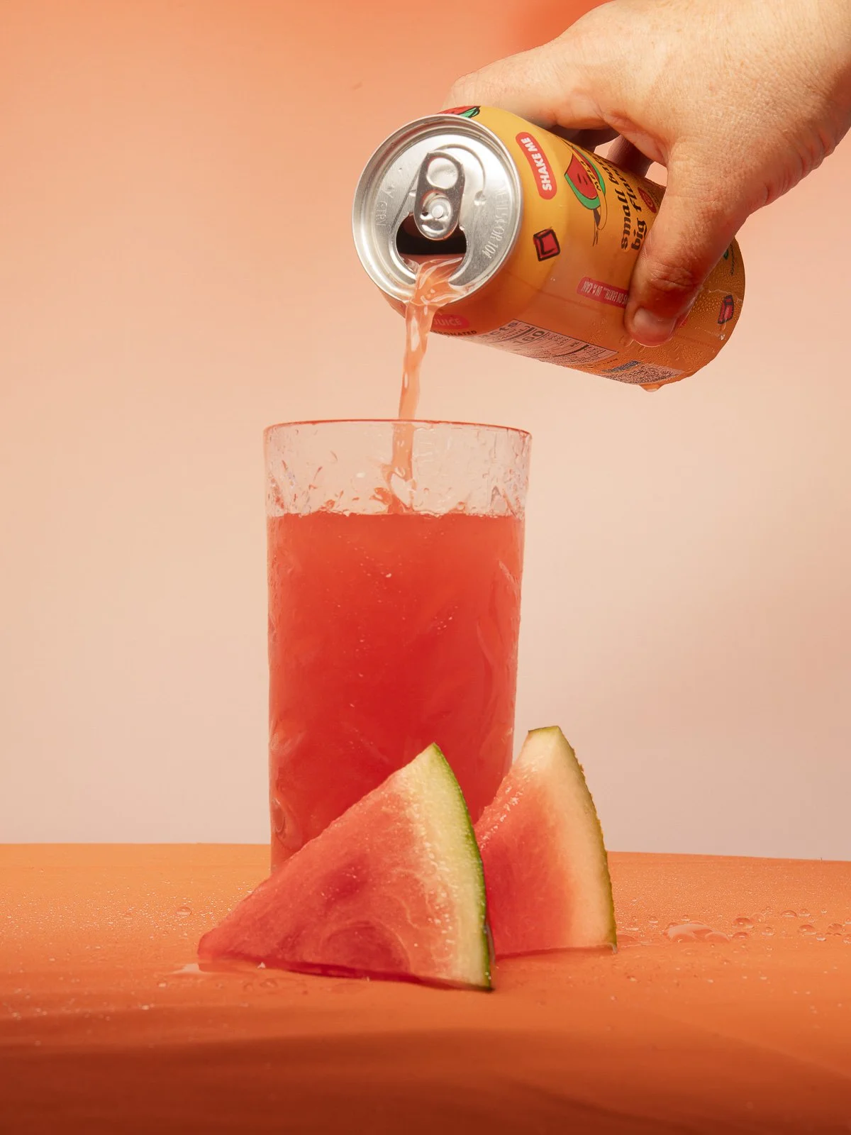 Watermelon drink being poured into a glass beside melon wedges.
