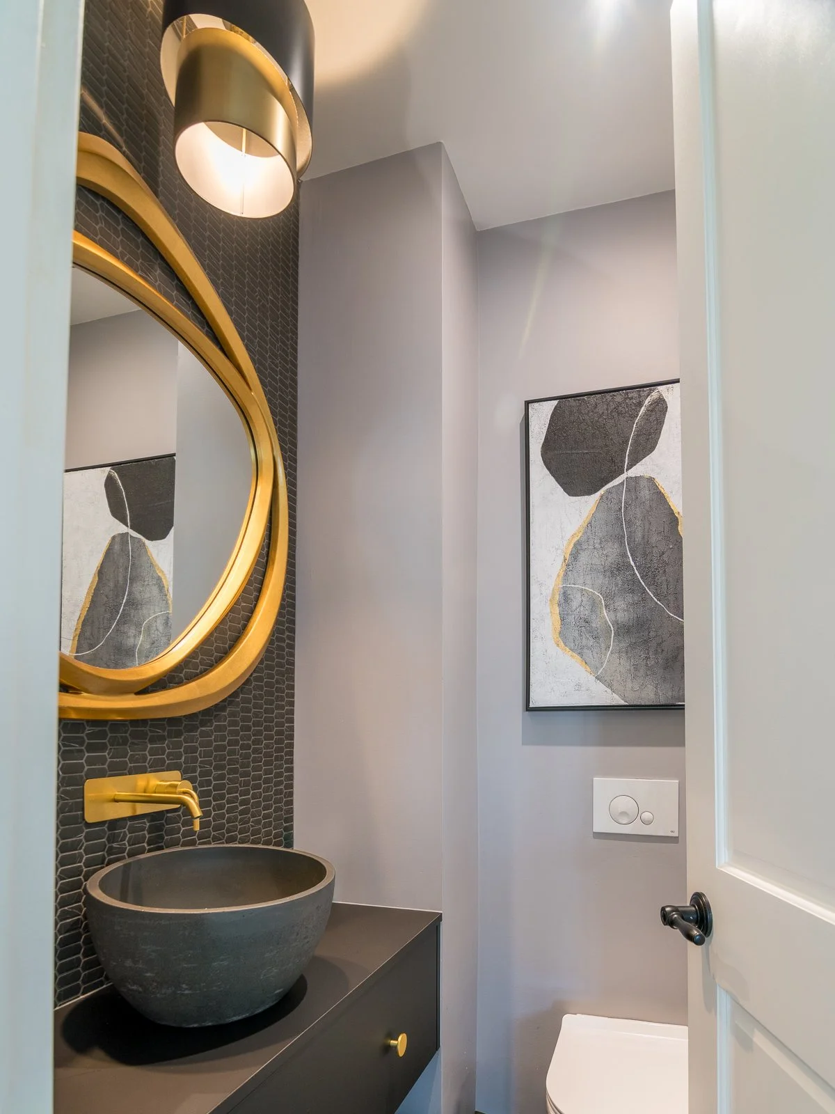 Detail Powder room with a round gold mirror, brass wall-mounted tap, and a concrete vessel basin on a dark floating vanity