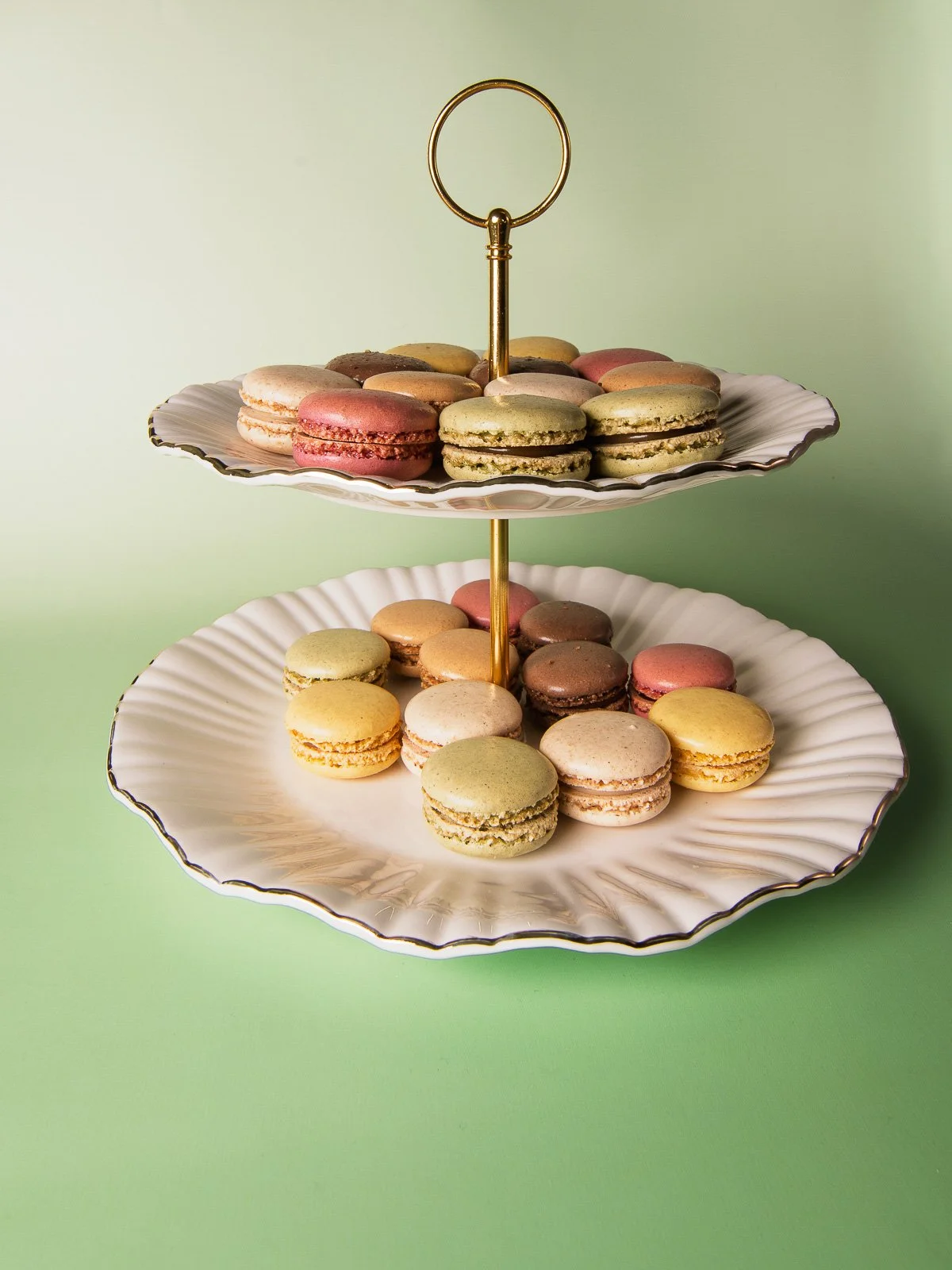 Macarons on a two-tier white cake stand against a green background.