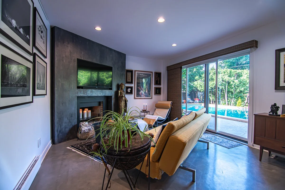 Living room with a concrete fireplace wall and a framed print wall, opening through sliding glass to the pool