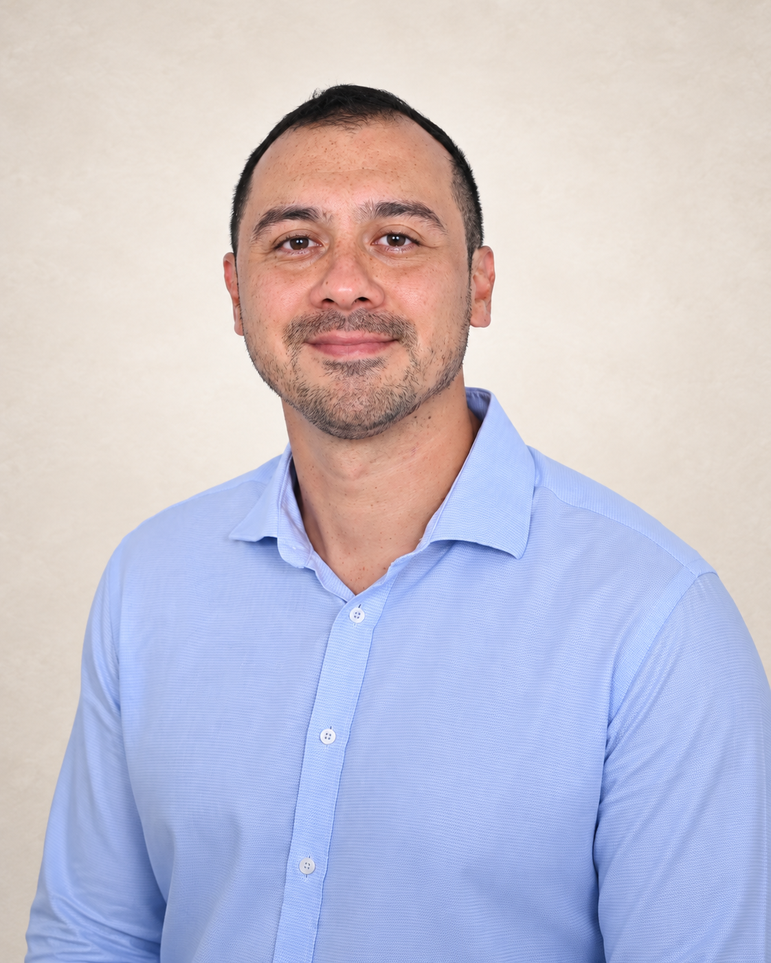 The founder of CallingCraft with short dark hair and light stubble wearing a light blue collared shirt, standing in front of a plain beige background.