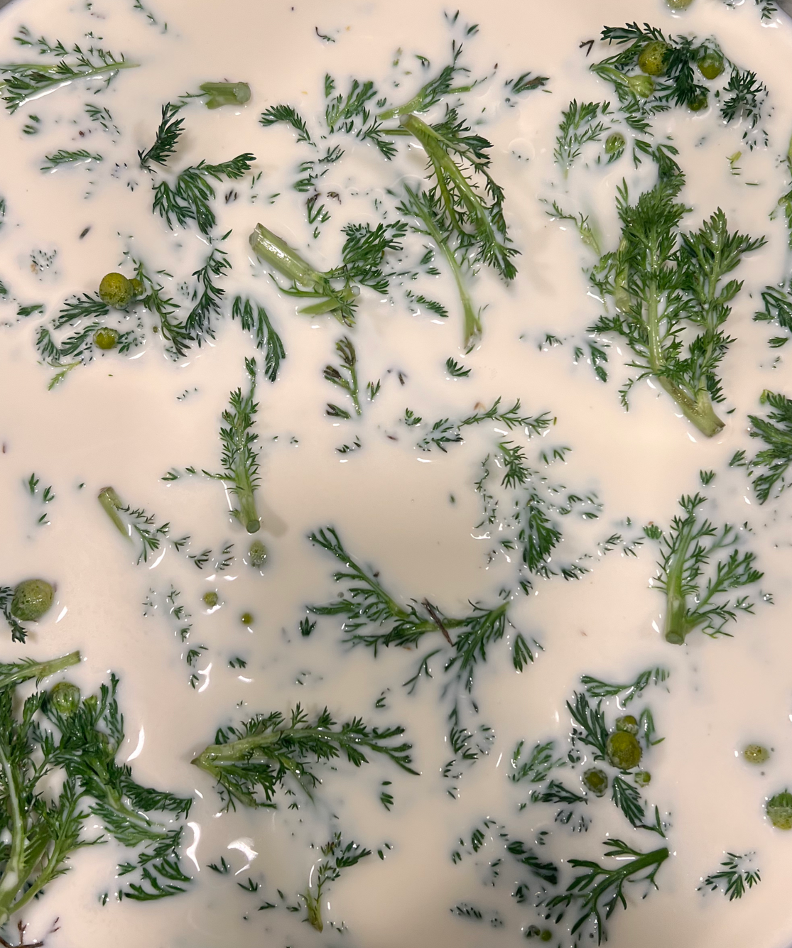 A mixture of fresh herbs and green peppercorns in a creamy liquid in a metal container.
