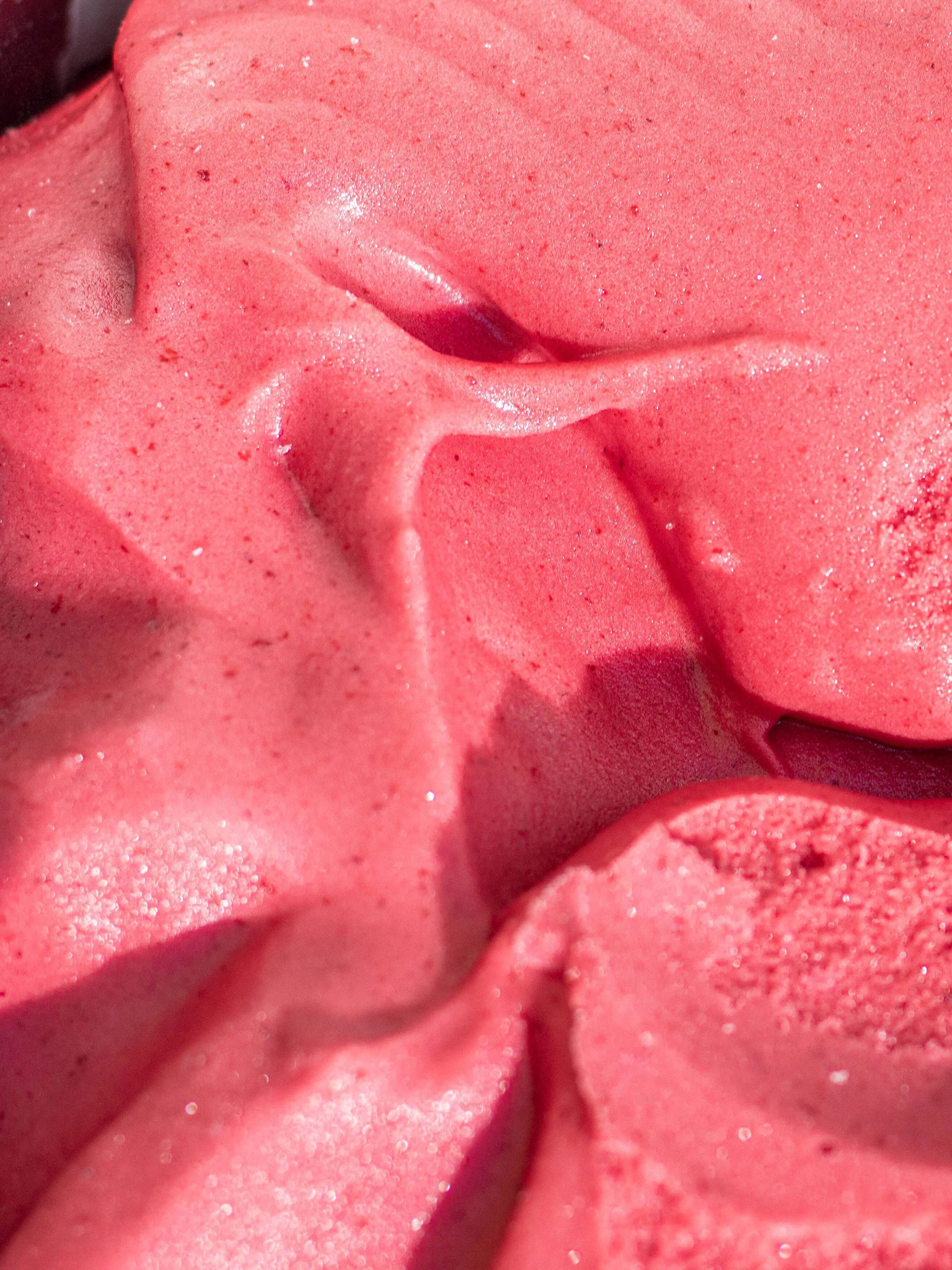 Close-up of pink and red frozen dessert with a smooth, creamy texture and small ice crystals.