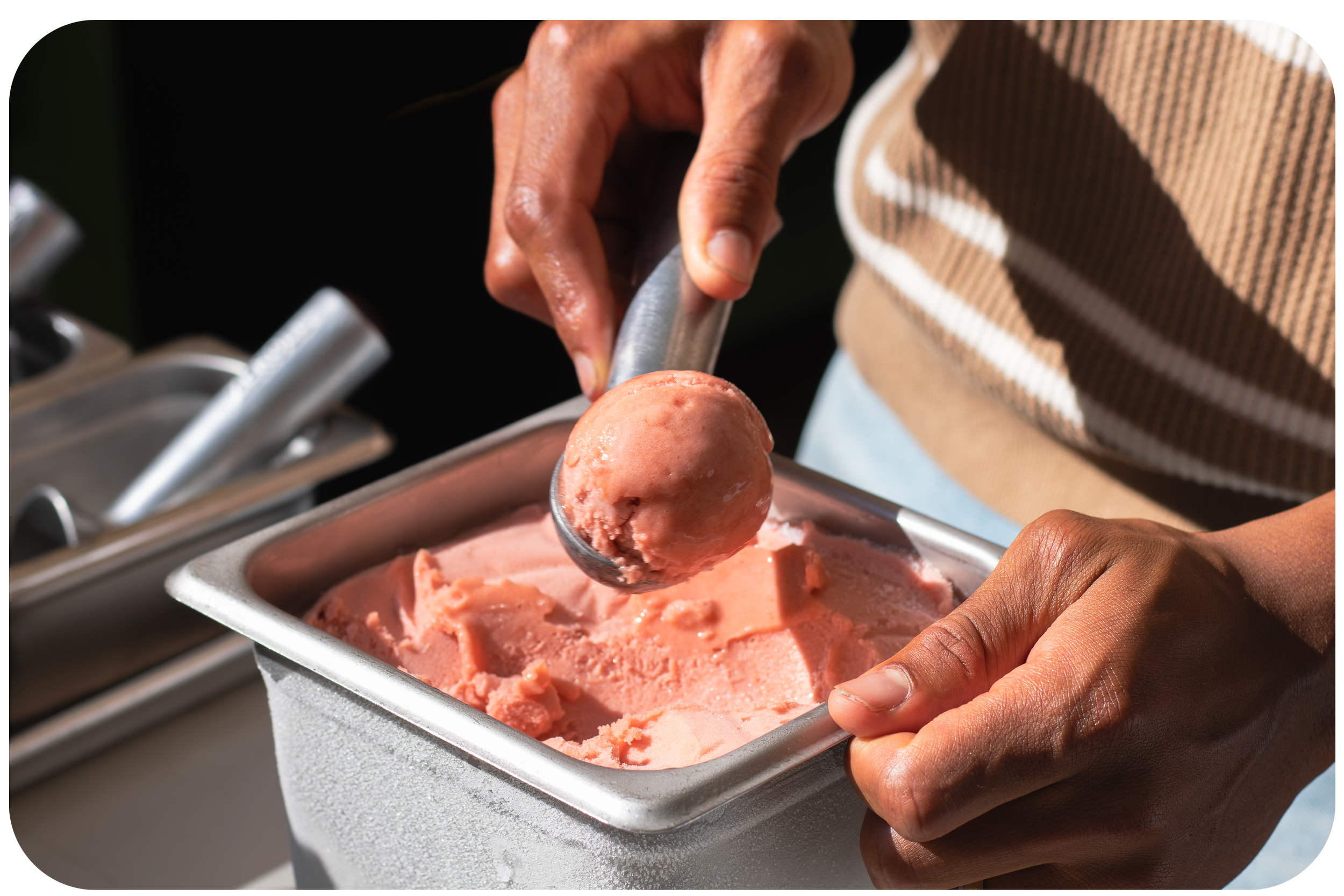A person serving pink ice cream from a metal container using an ice cream scoop.