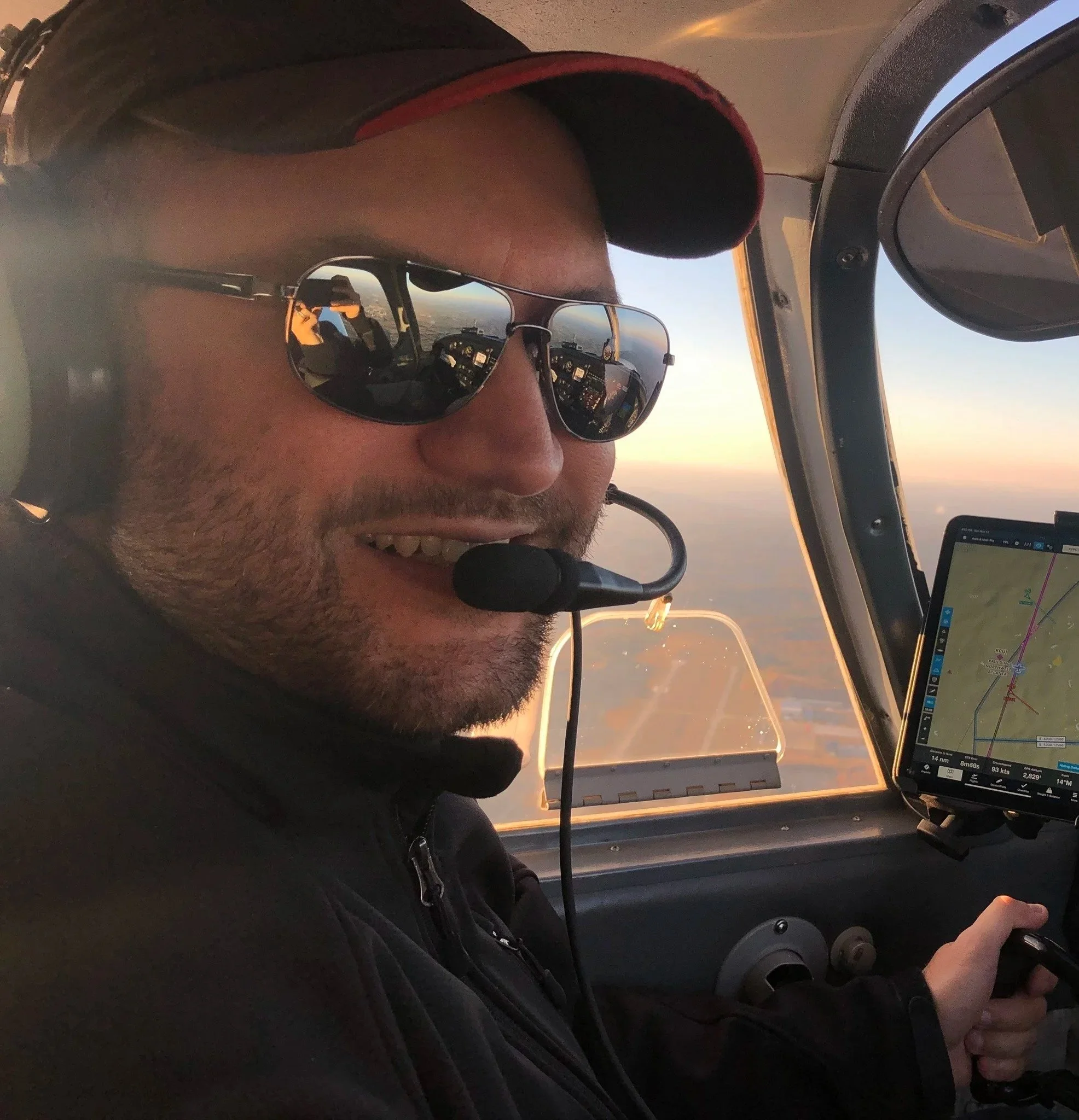 Attorney Mahmoud Khatib wears sunglasses and an aviation headset while flying an aircraft during sunset, with the instrument panel visible.