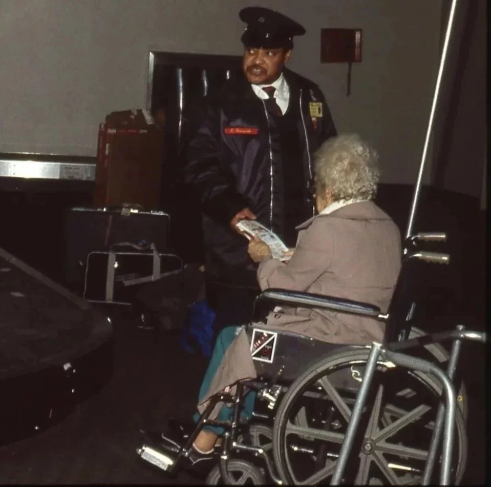 A police officer talking to an elderly woman in a wheelchair, exchanging money in a parking garage.