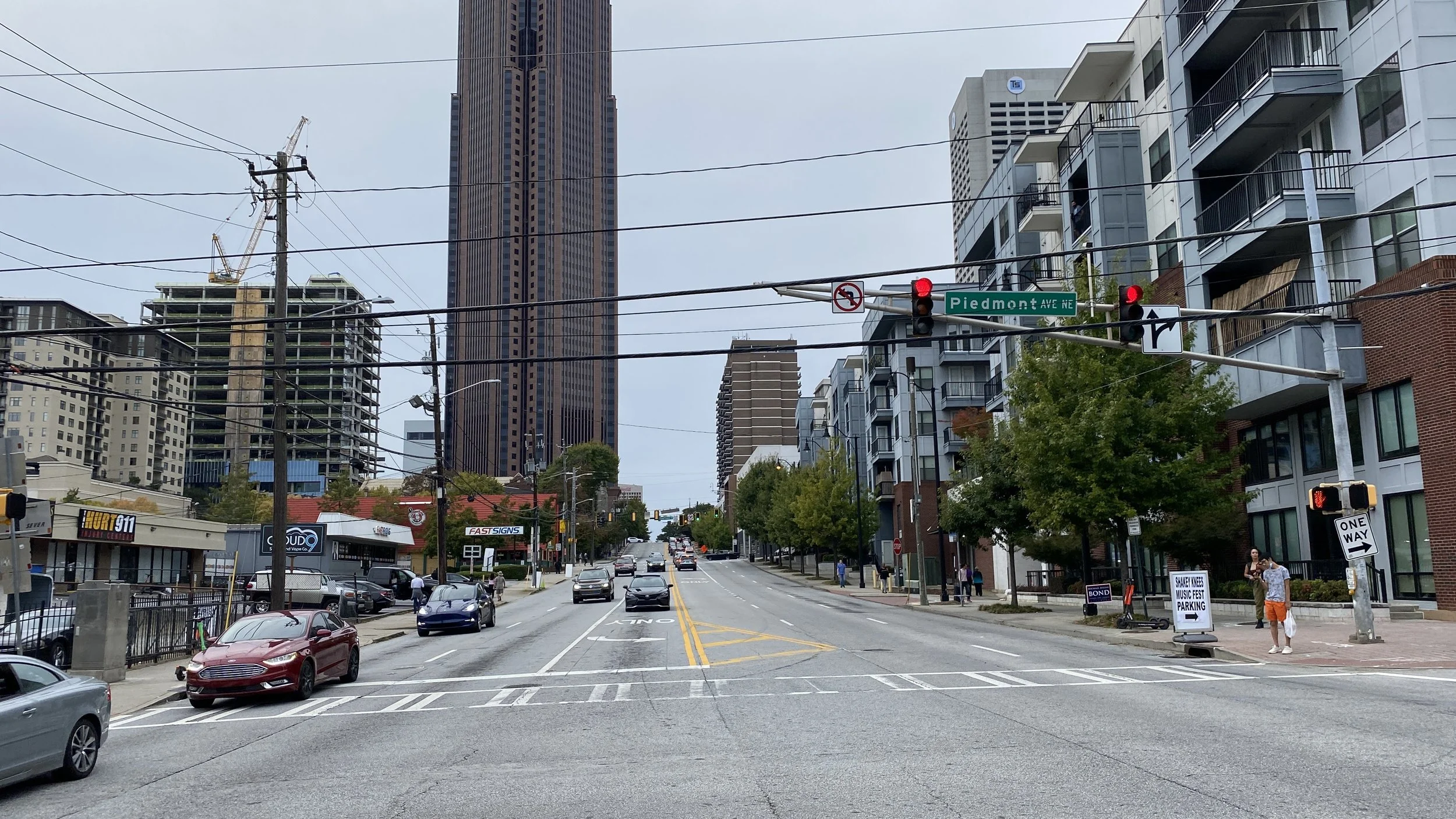 Street scene in an urban Atlanta area with tall buildings, cars on the road, pedestrians on the sidewalk, traffic lights, and street signs. The street sign reads 'Piedmont Ave NE'.