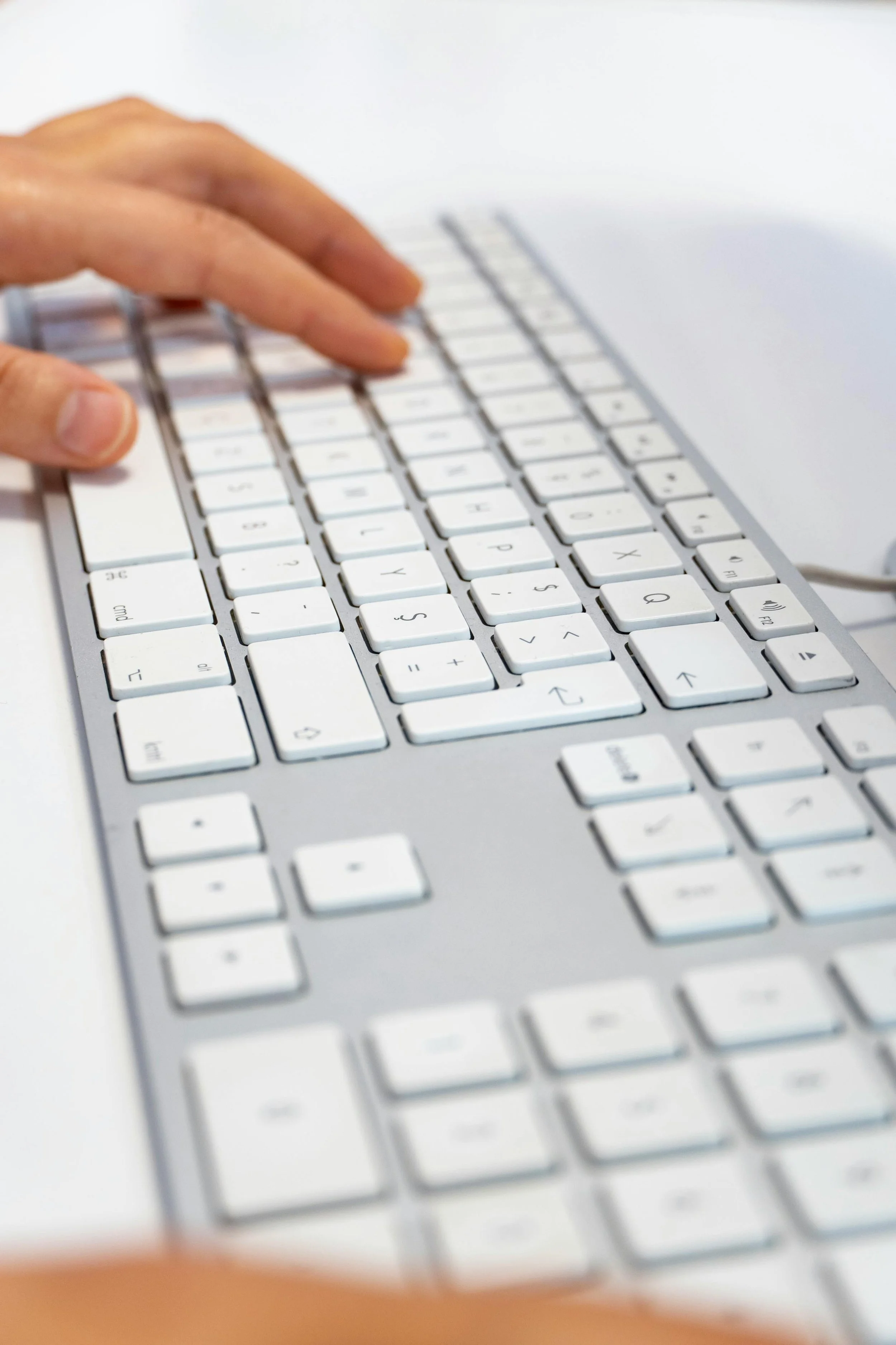 Close-up of a hand typing on a white computer keyboard with a white background.