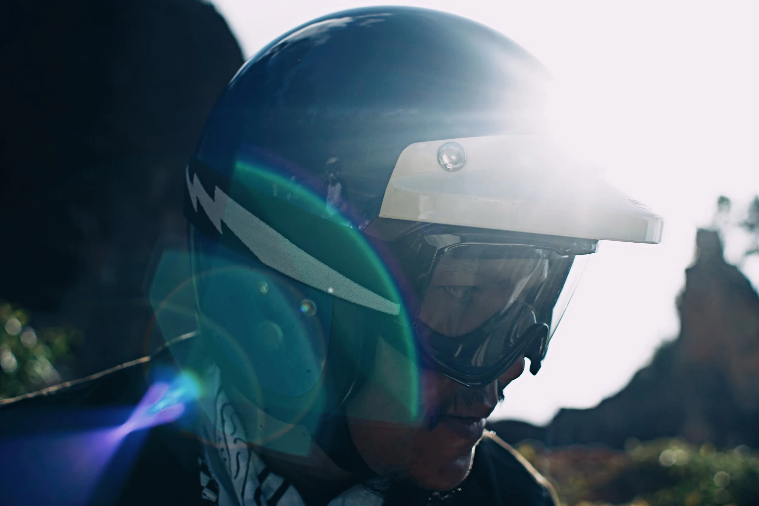 A person wearing a motorcycle helmet outdoors with sunlight glare and lens flares.