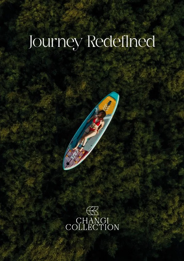 An aerial view of a woman in a red swimsuit lying on a paddleboard surrounded by lush green trees. The text 'Journey Redefined' is at the top, and 'Changi Collection' logo is at the bottom.
