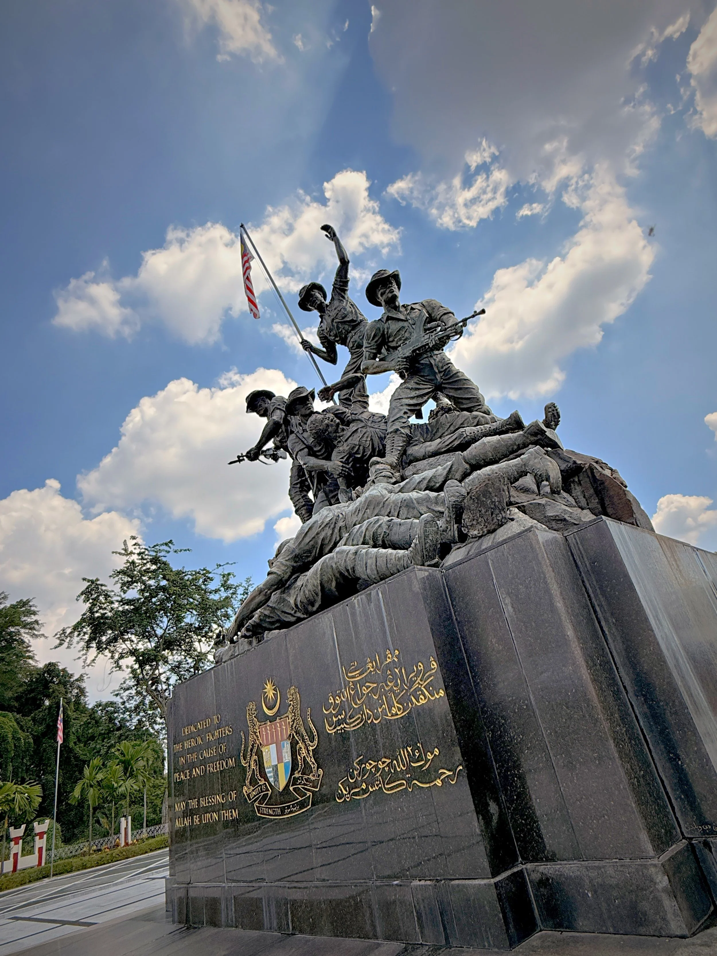 Monument with a group of soldiers and a flag, with a black plaque featuring gold Arabic and English inscriptions, dedicated to the hero flight fighters.