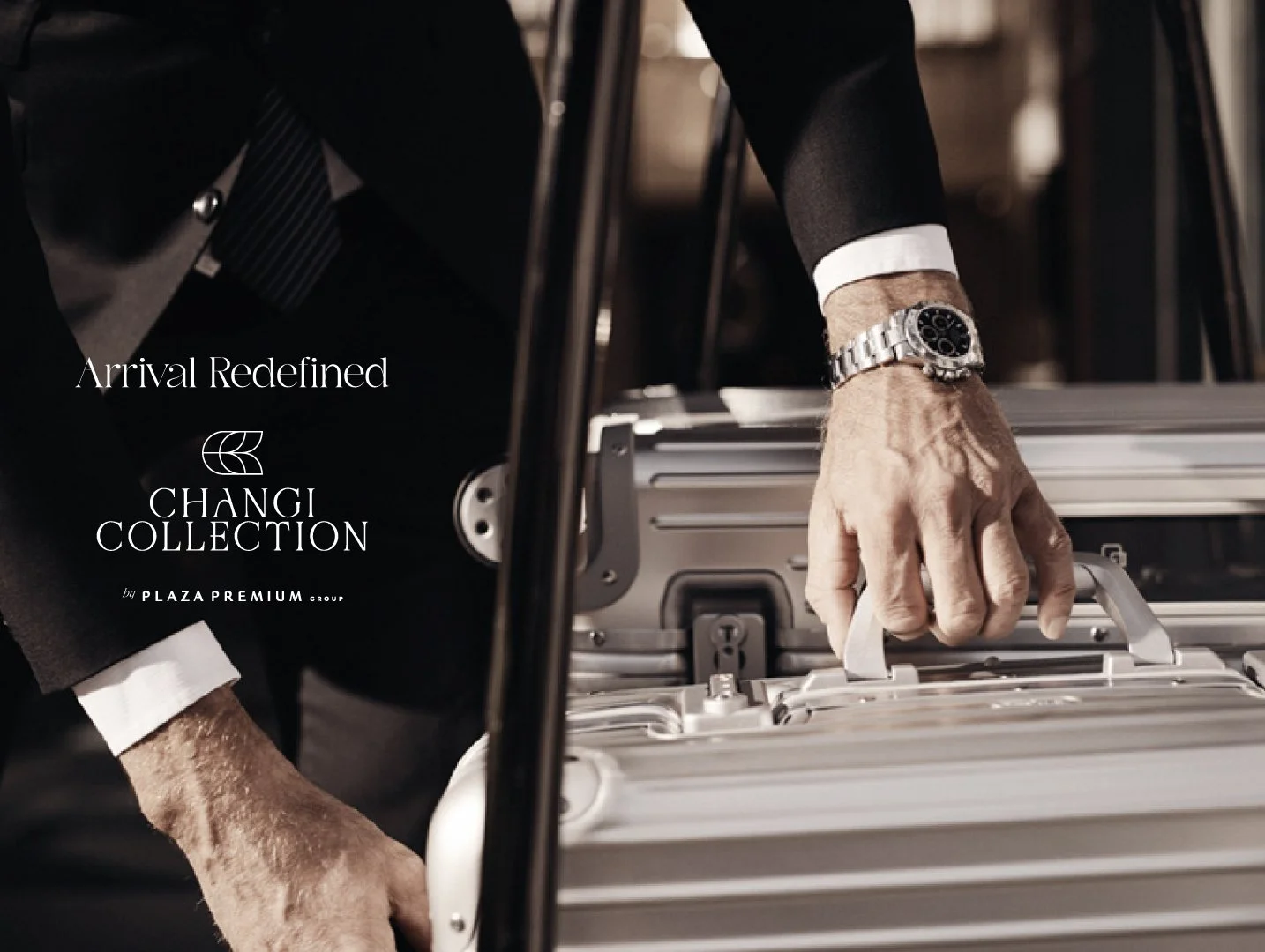 Hand of a man in a black suit with a silver watch, placing a briefcase on a luggage cart.