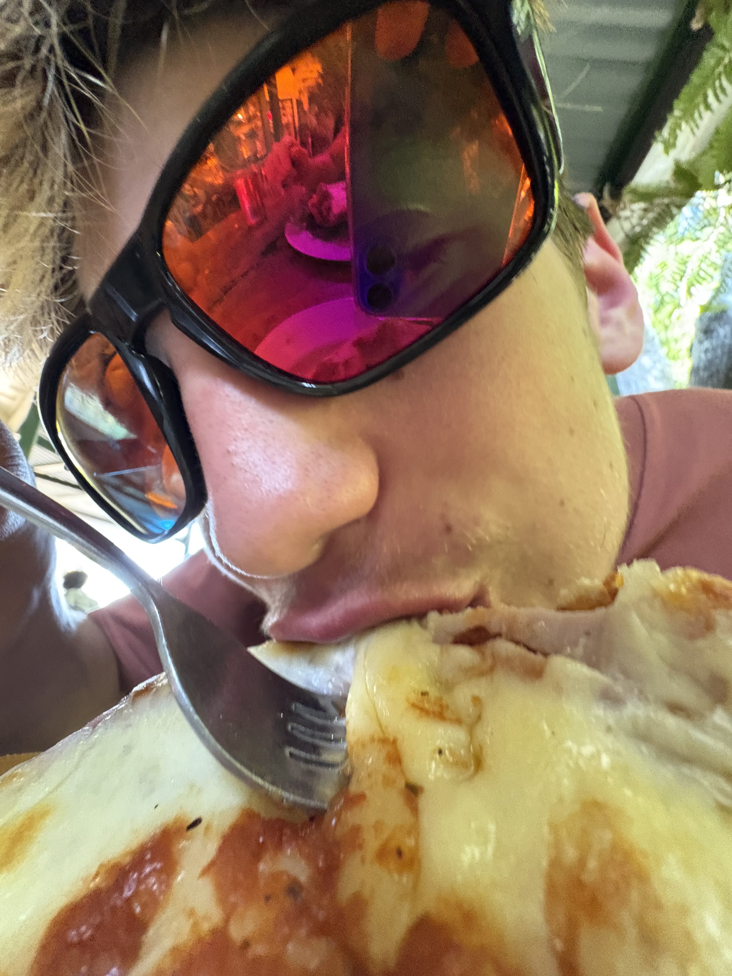 Person wearing large sunglasses eating a slice of pizza
