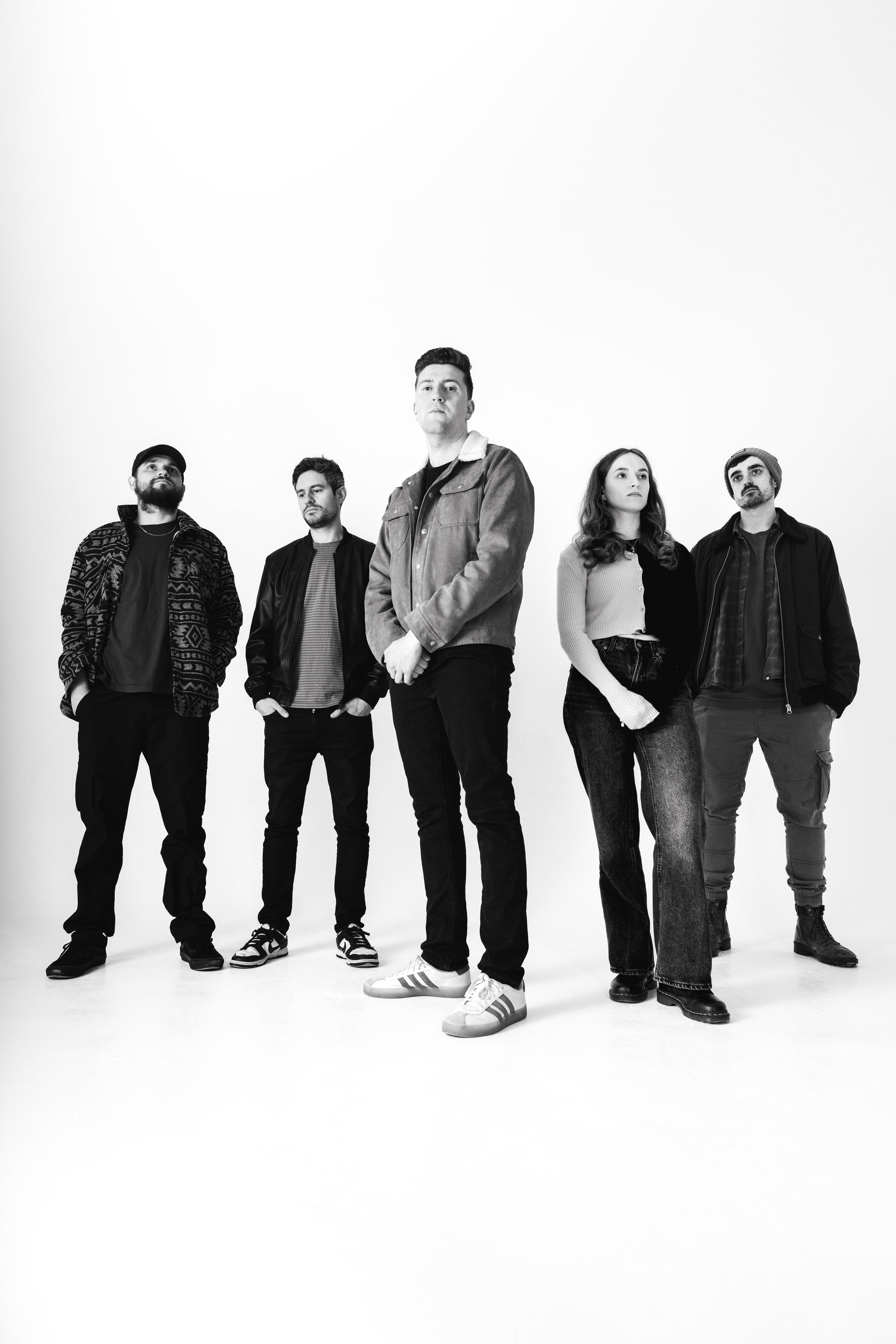 Black and white photo of five people standing against a plain white background, dressed in casual clothing, with serious expressions.