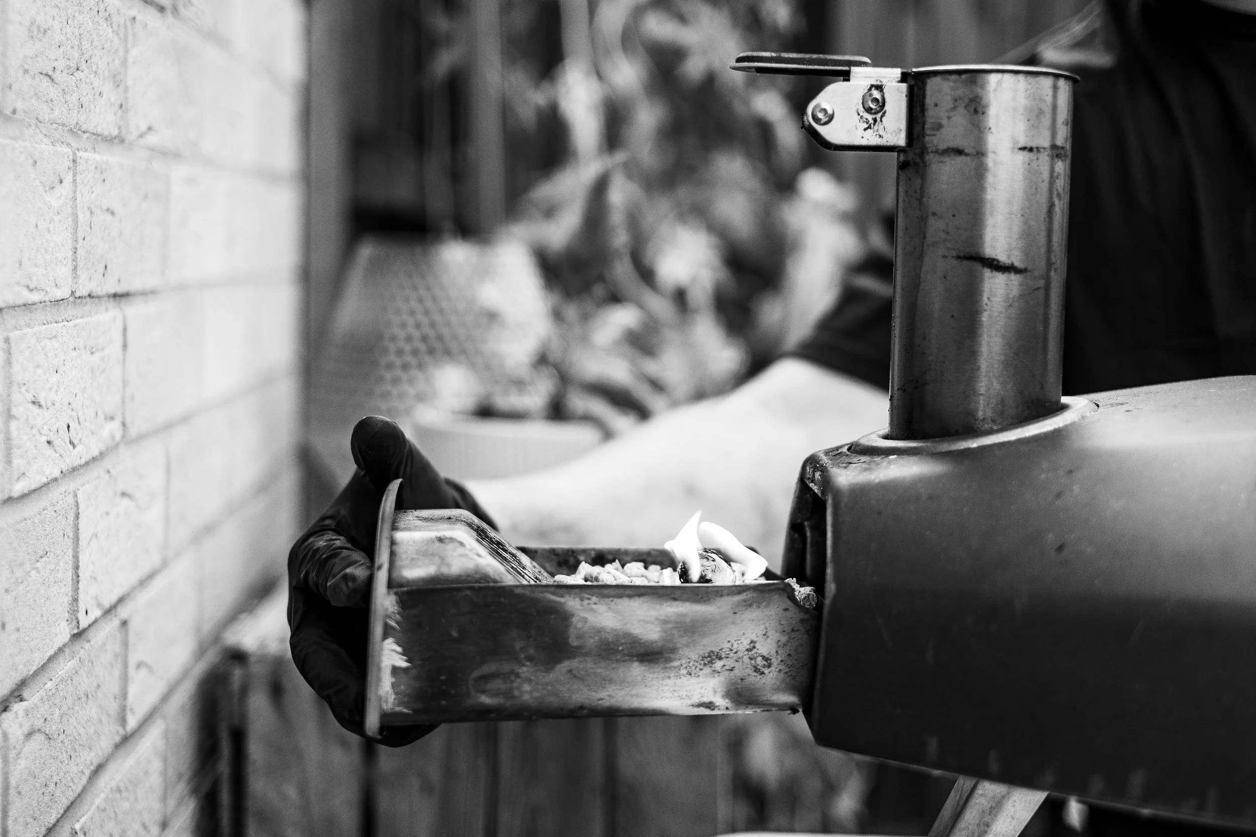 Close-up of a hand wearing a glove, placing lit wood into a pizza oven