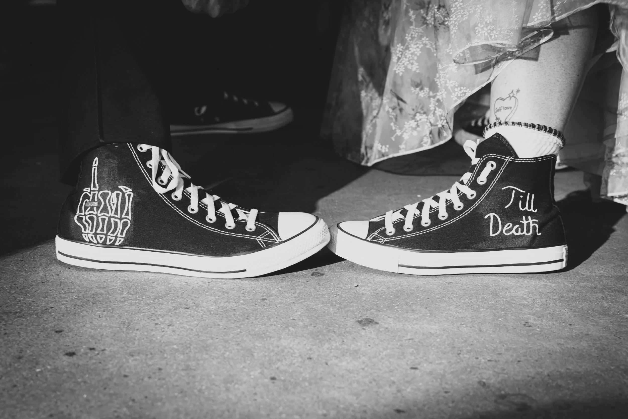 Close-up of people wearing black high-top sneakers with white laces, with patches reading 'Till Death'.