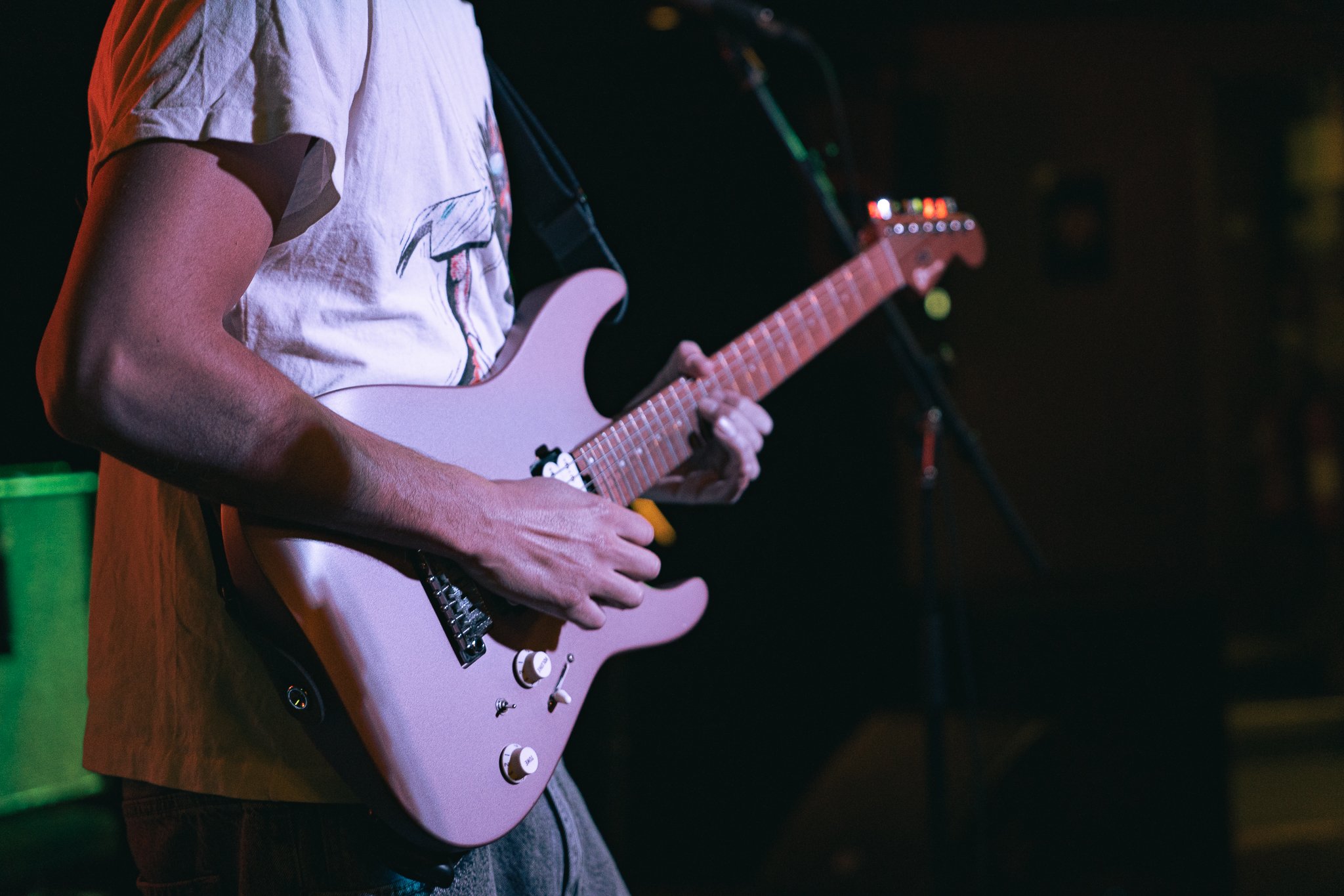 A person is playing a pink electric guitar in a dimly lit setting, possibly during a performance or practice session.