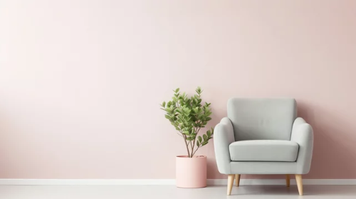 A gray armchair next to a potted green plant in a pink pot against a light pink wall.
