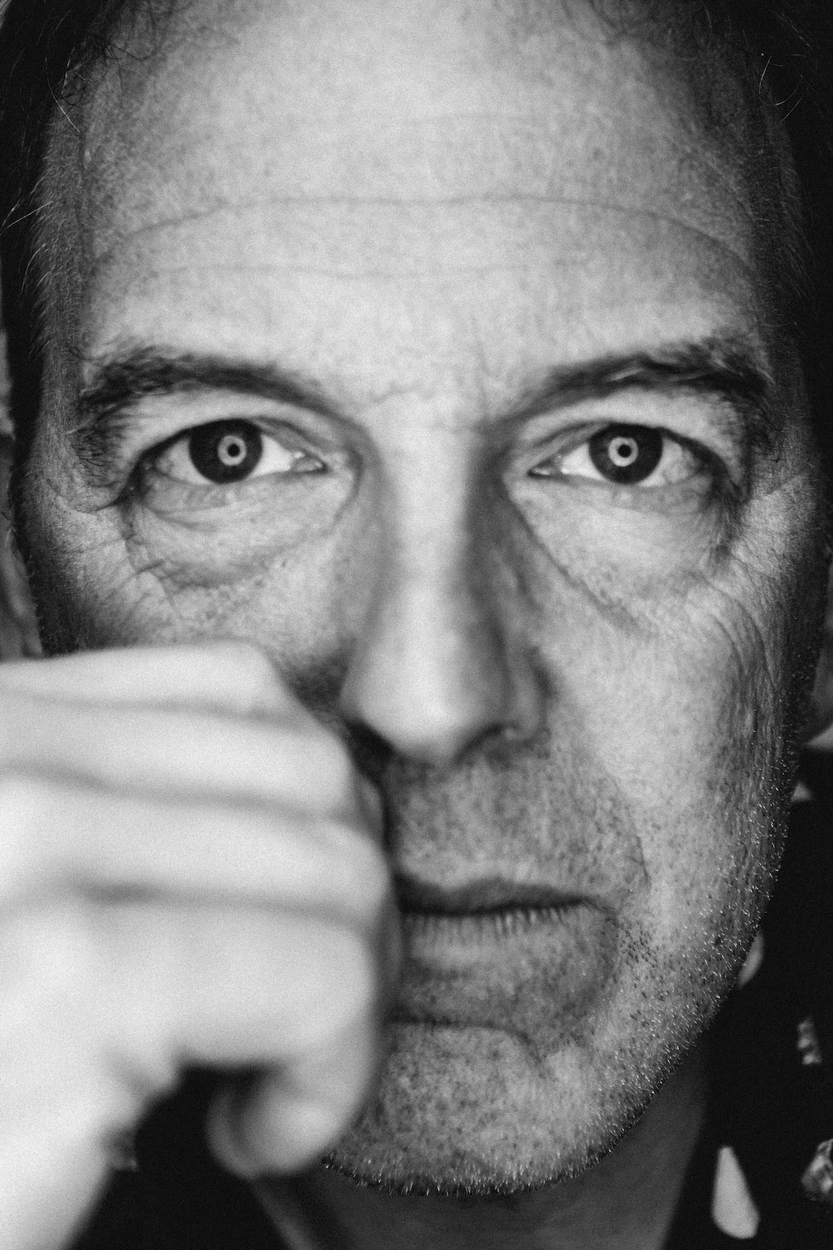 Close-up black and white portrait of a man with intense expression, partially covering his face with his hand.