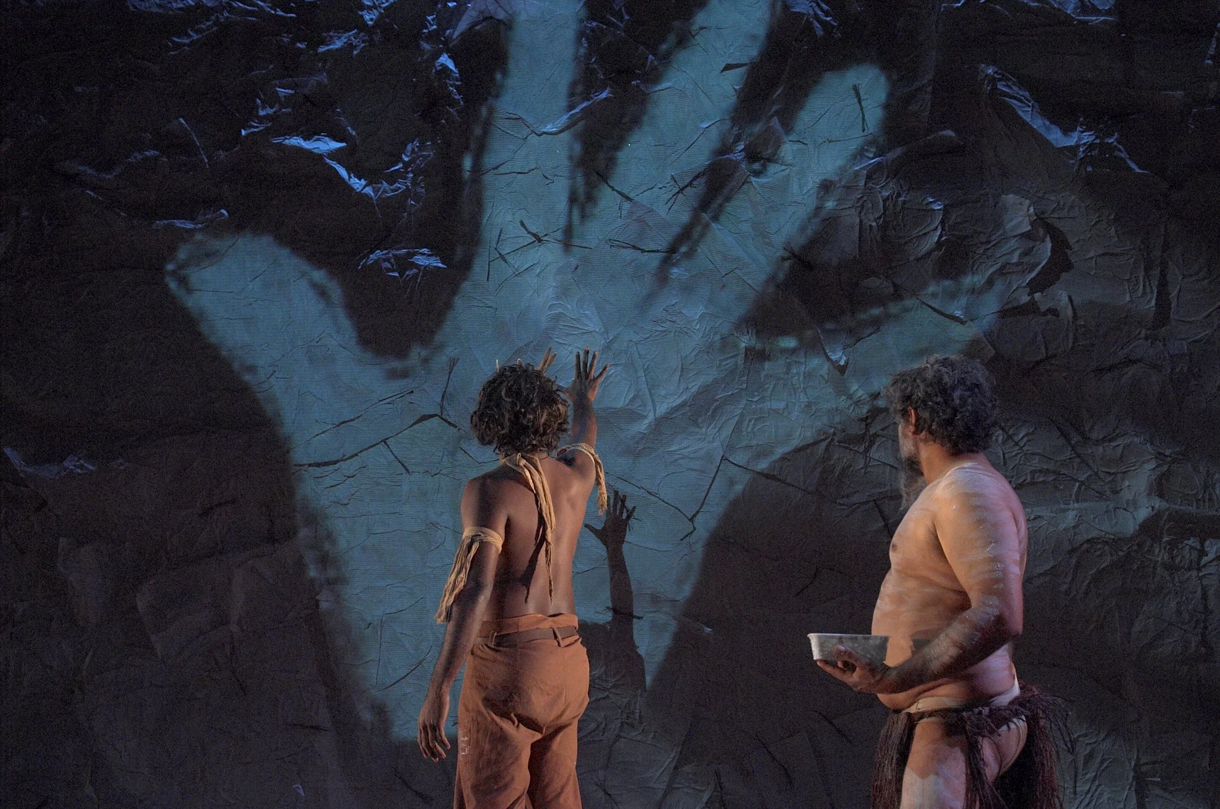Jimi Bani and Kelton Pell in the world premiere performance of Jandamarra. The two men look at a projected image of a huge animated hand.