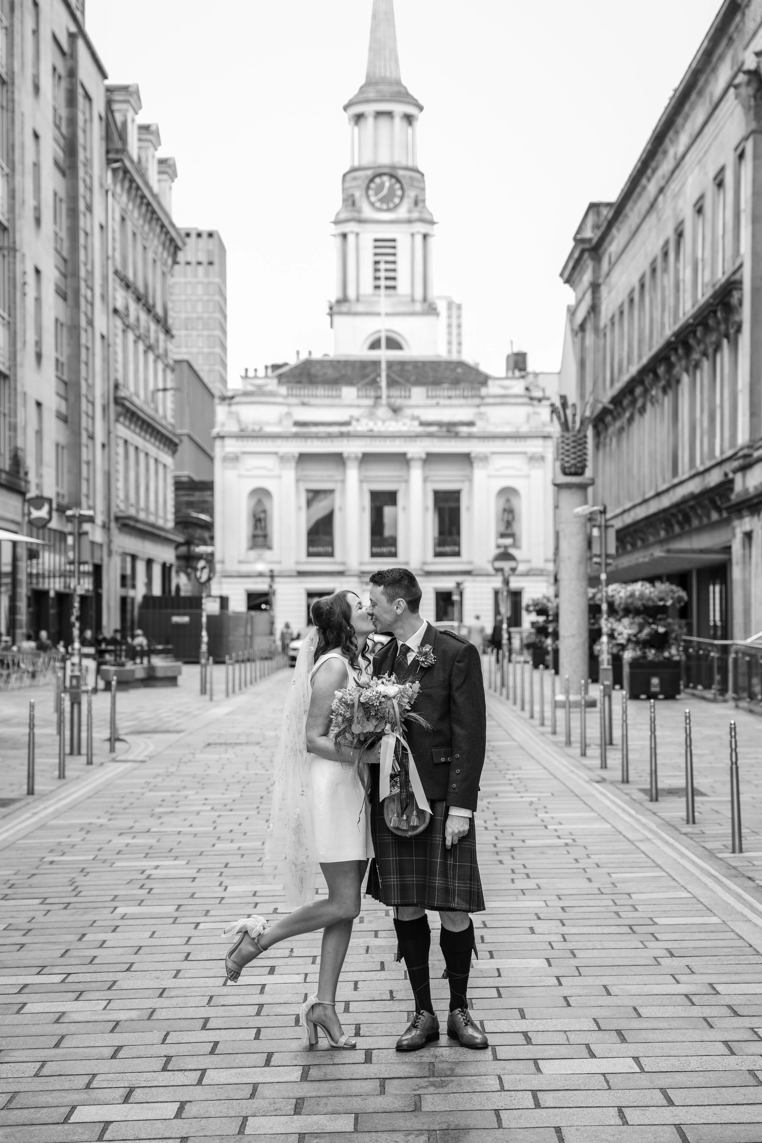 Wedding in Glasgow city centre, Bride and groom kissing with the brides leg kick up backwards edited in Black and White