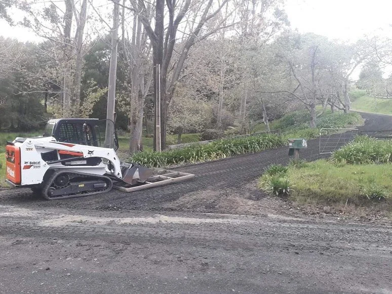 Skid-steer loader with leveling bar smoothing out gravel driveway.