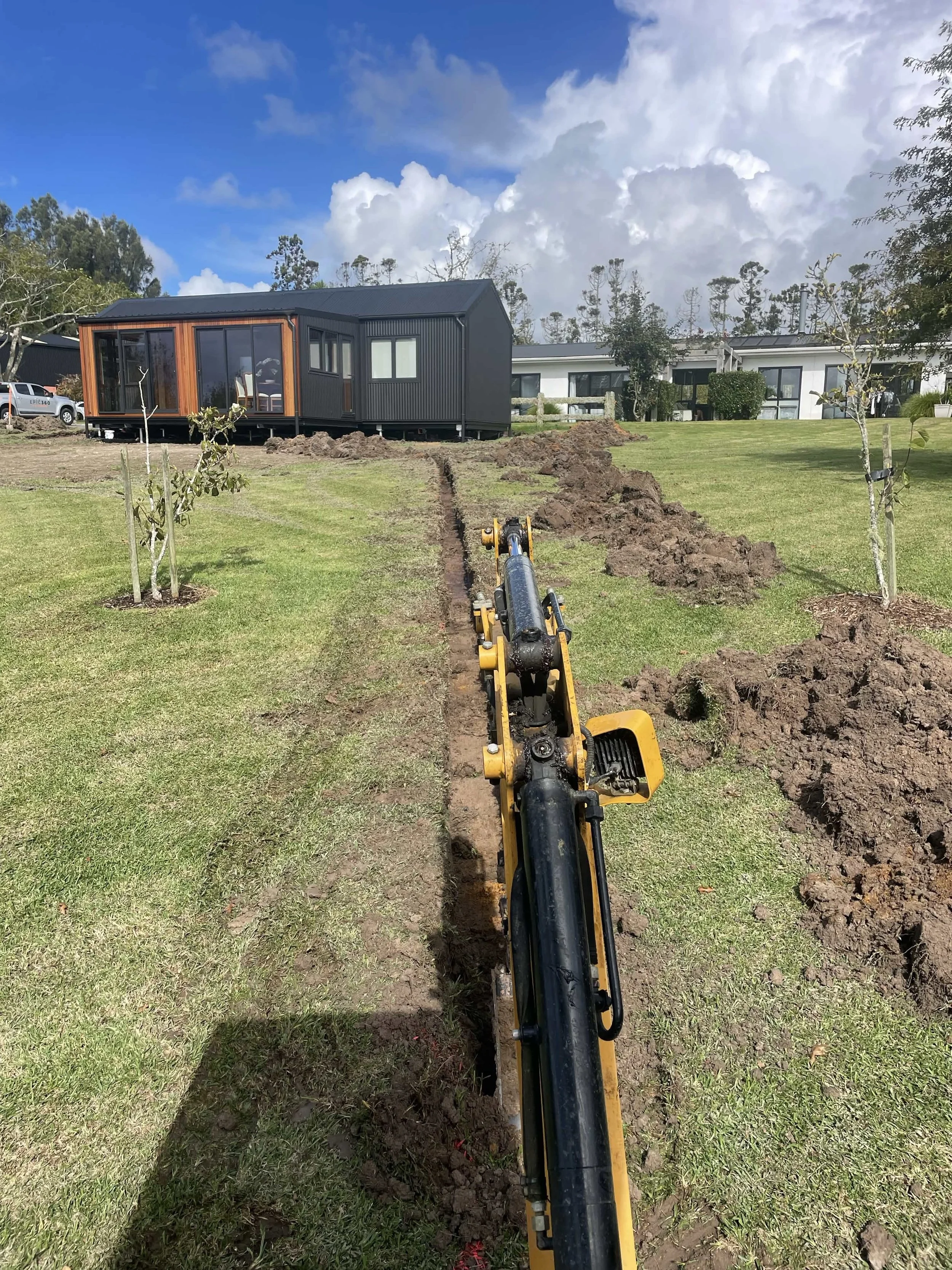 a trench is being dug with a small excavator to install a stormwater runoff drainage system