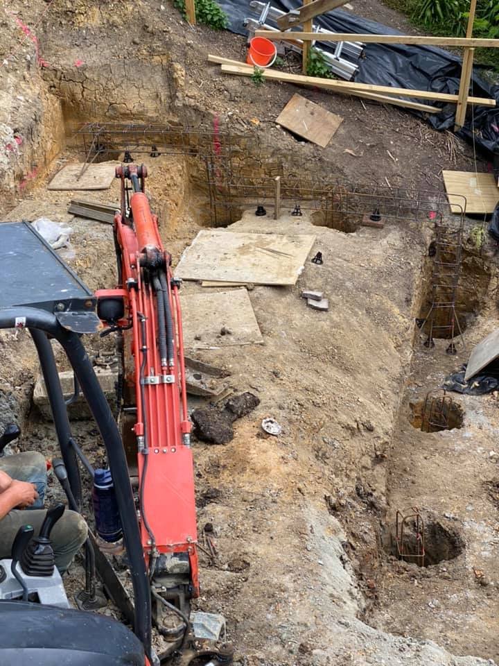 Construction site with an excavator digging a foundation, with rebar and concrete forms in place.