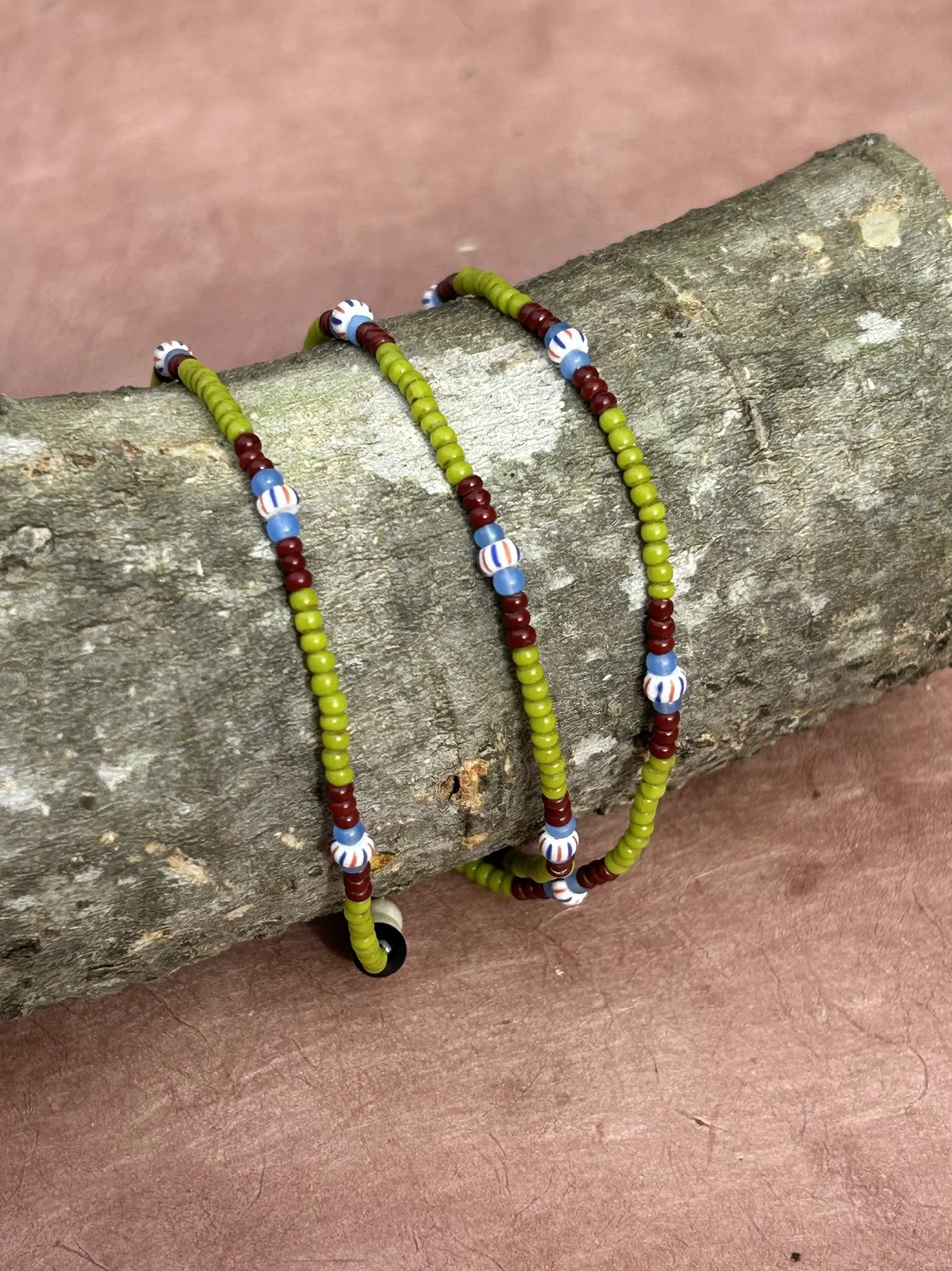 Colorful beaded necklaces hanging on a rough tree trunk.