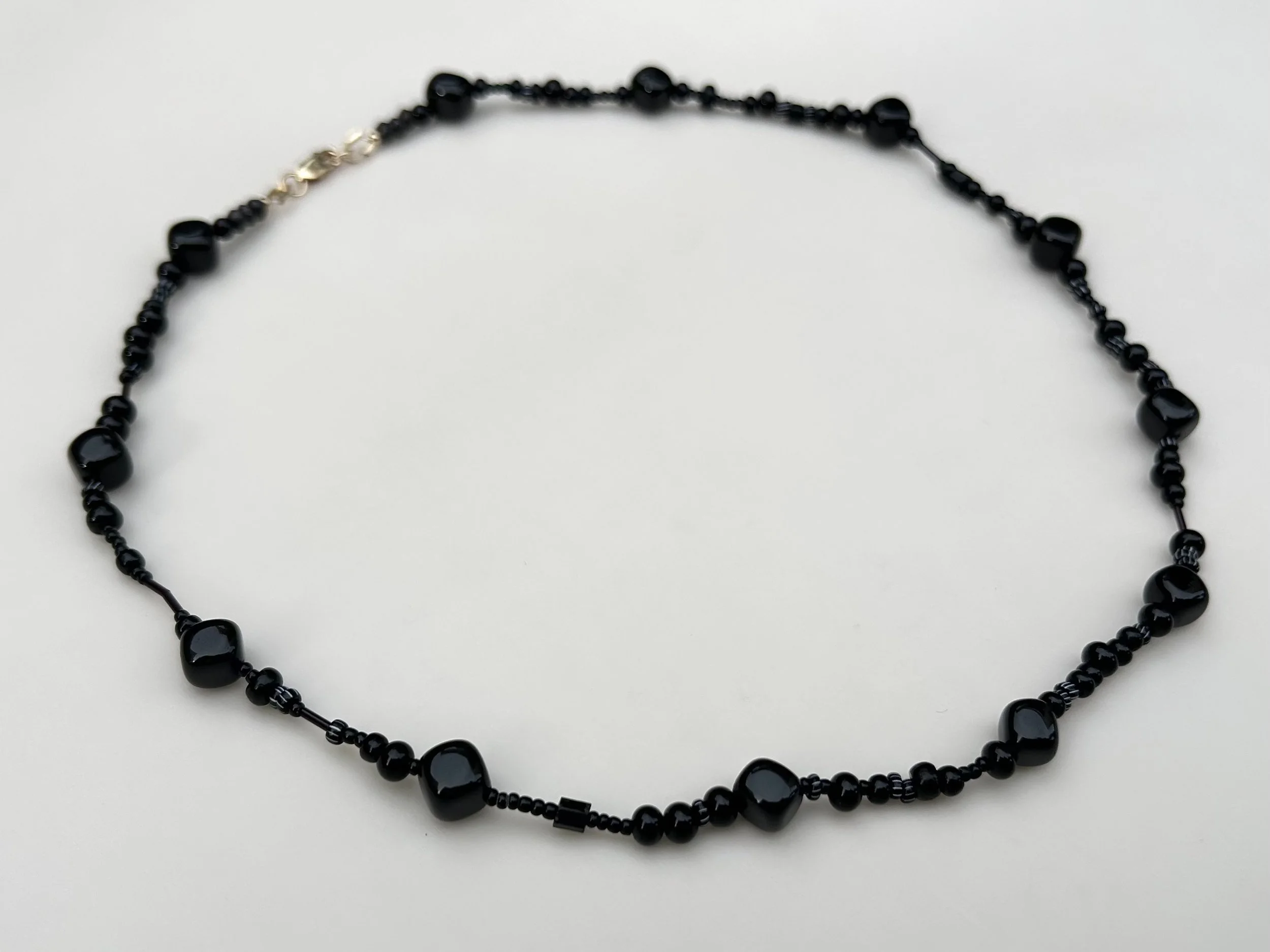 Black beaded necklace with gold accent on a white background.
