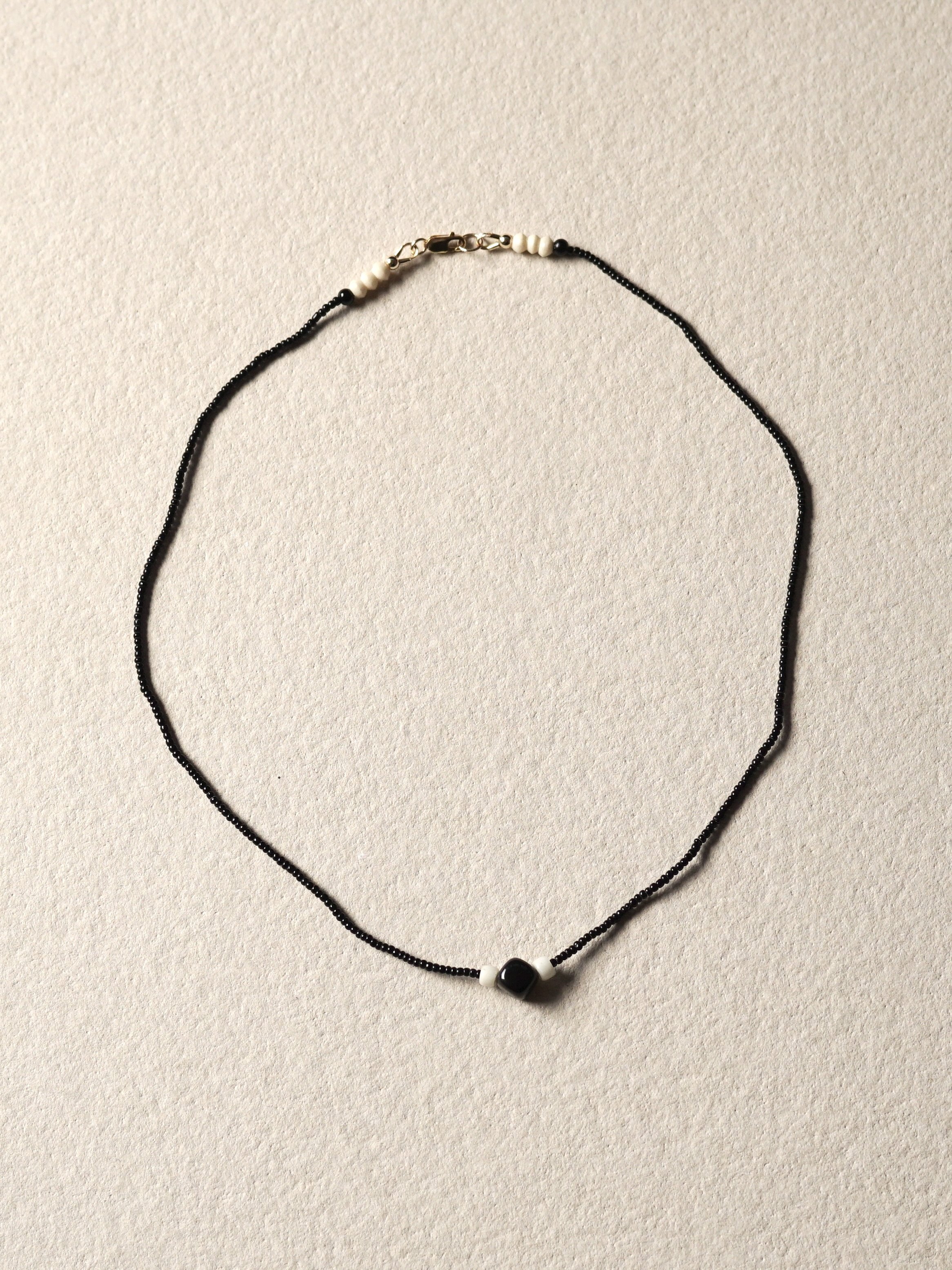 An antique black beaded necklace with white and black beads and a larger black bead in the center, arranged on a beige background.