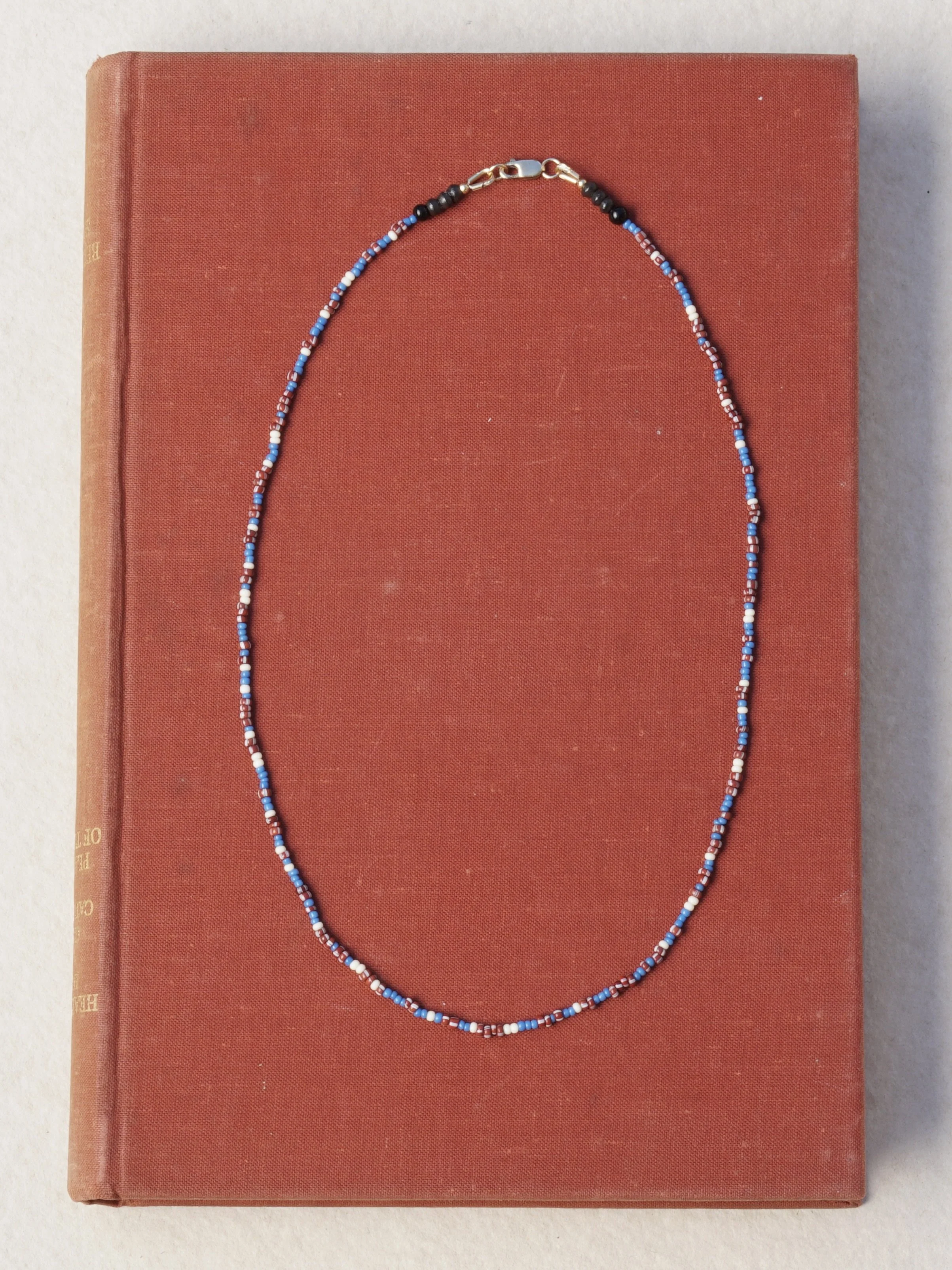 A beaded necklace with blue, white, red, and black beads lies on a closed orange book with a textured cover.