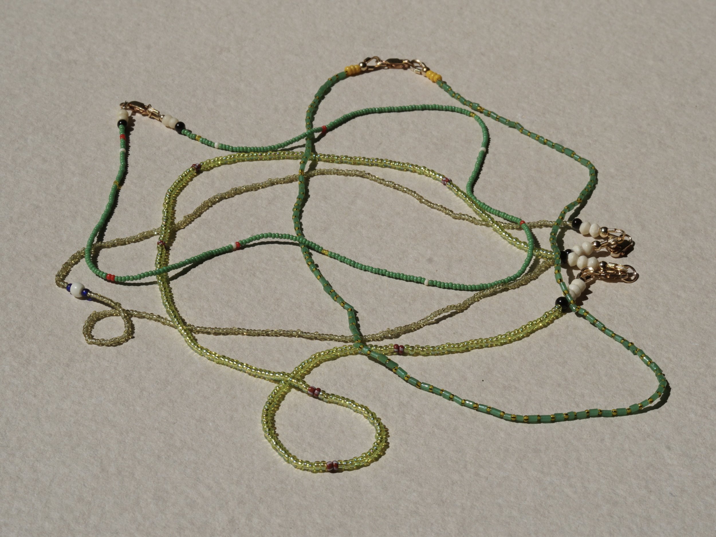 Multiple beaded necklaces and bracelets in various colors, including green, yellow, white, black, and red, are arranged on a light-colored surface.