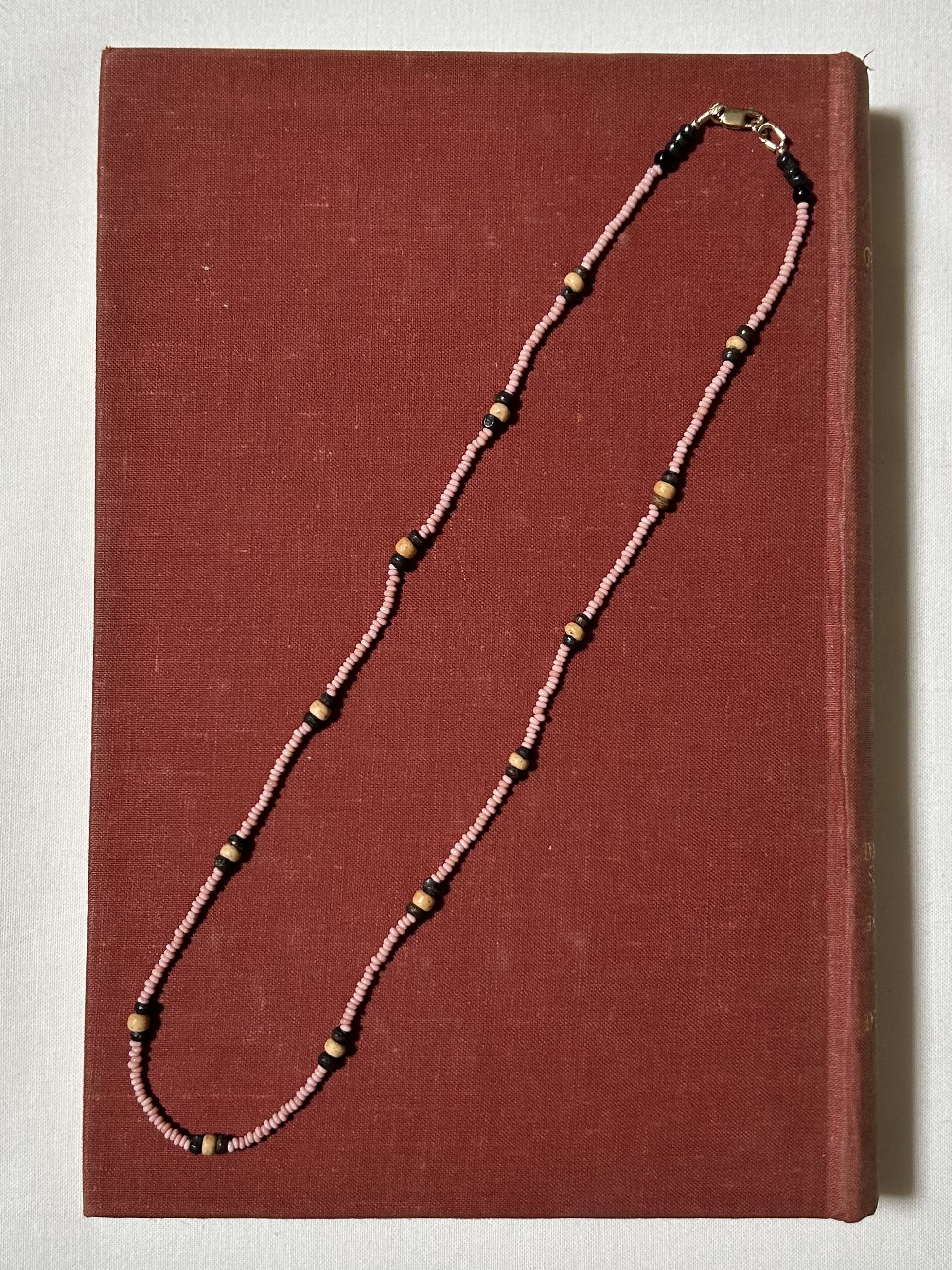 A beaded necklace with pink, black, and cream-colored beads draped over a red hardcover book placed on a white surface.