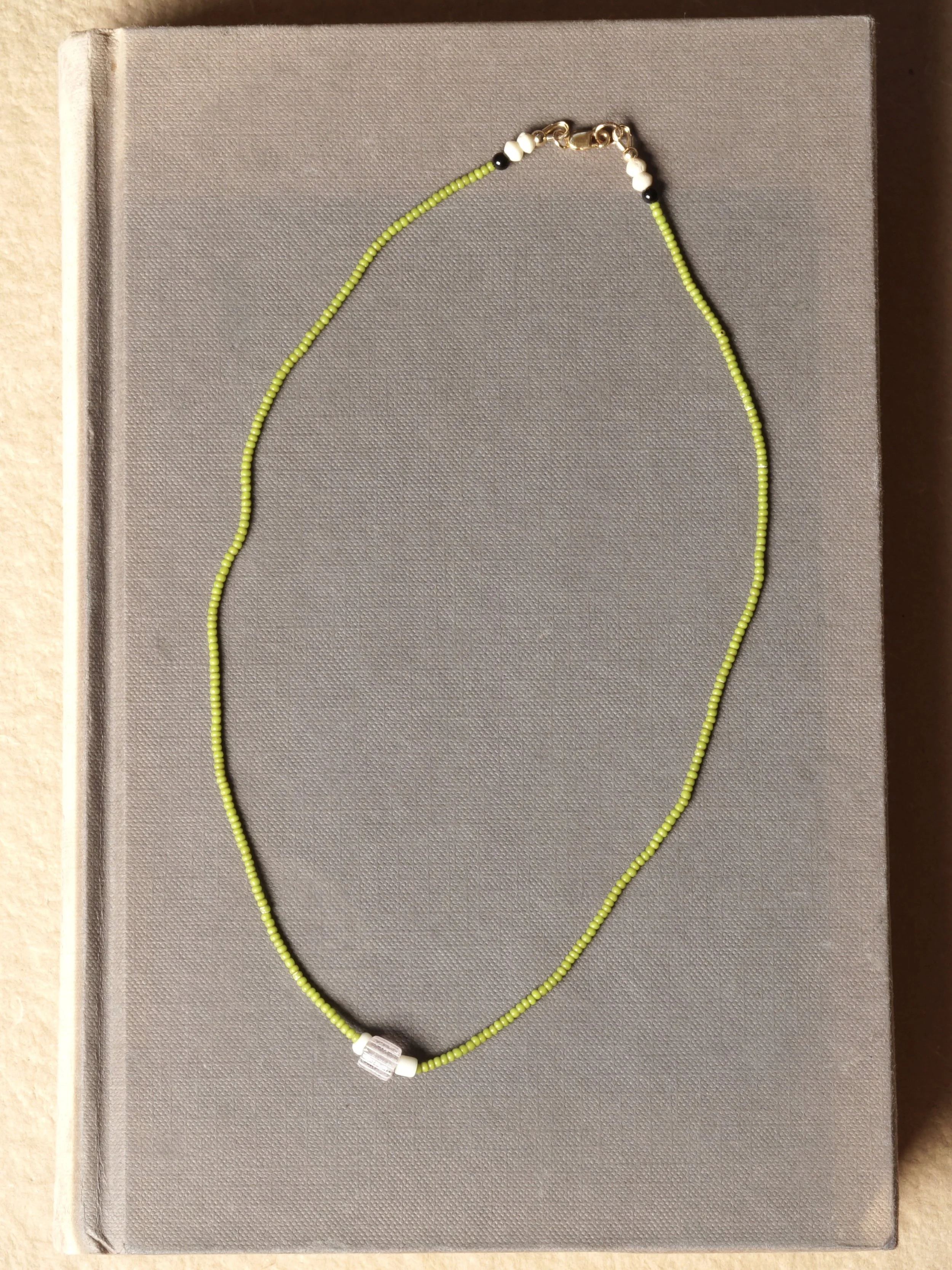A beaded necklace with bright olive green, white, black, and gold beads resting on an antique book