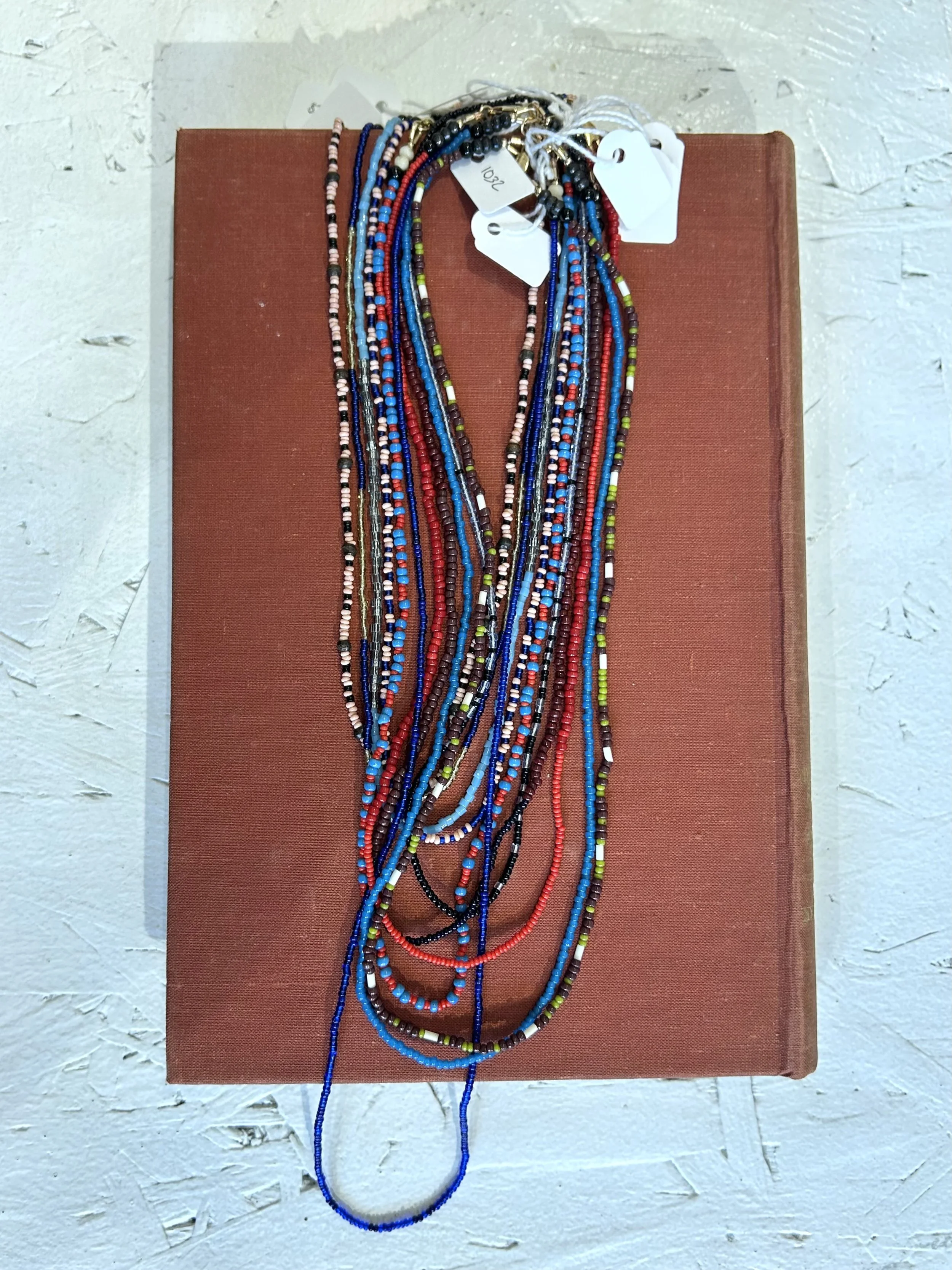 Multiple colorful beaded necklaces arranged on a red book, set against a white textured surface.