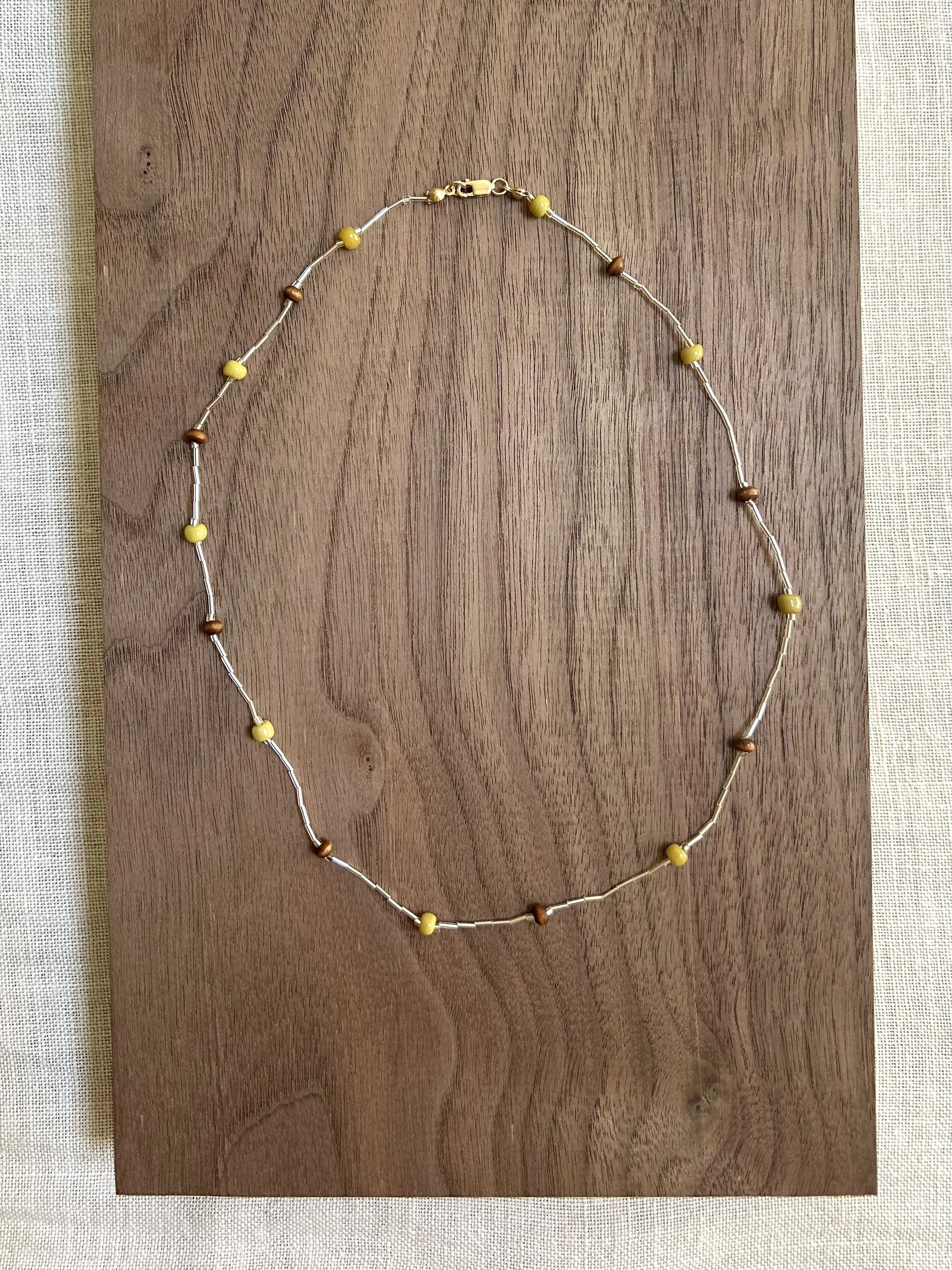 Beaded necklace with yellow and brown beads on a wooden board.