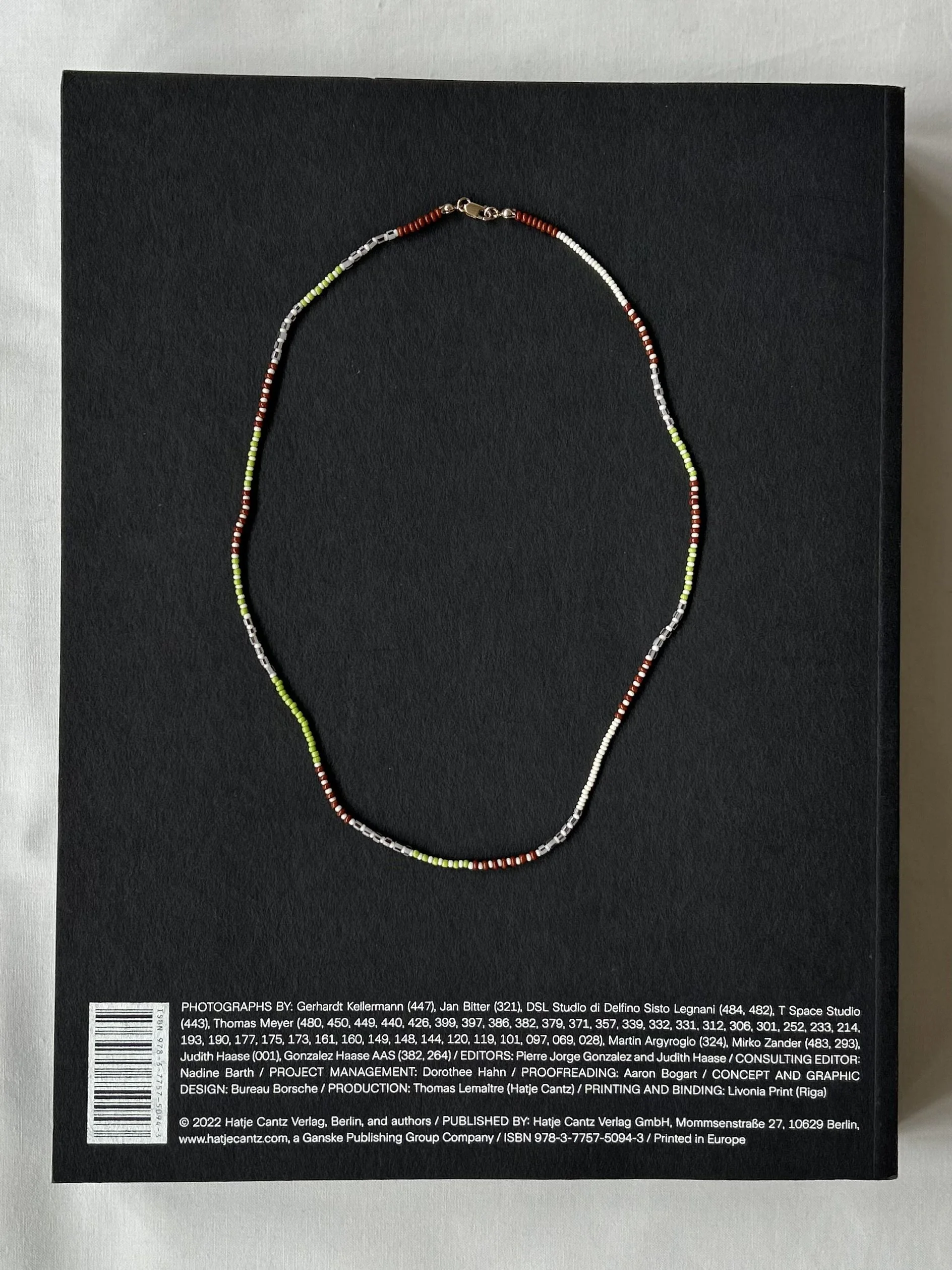 A beaded necklace with multicolored beads in shades of red, white, white, green, and silver, laid on a black background.