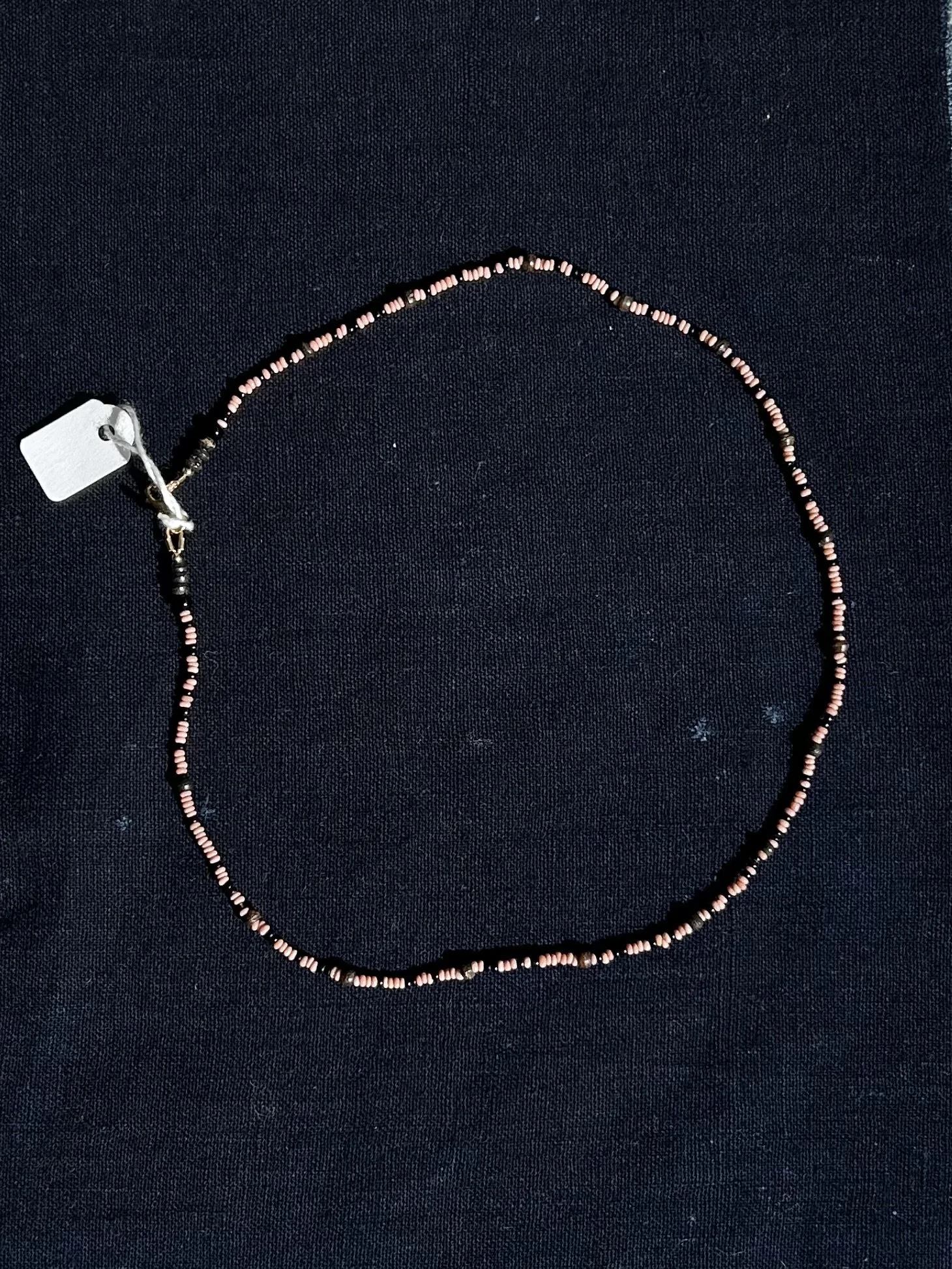 Close-up photo of a beaded necklace with a small white tag attached, displayed on antique Japanese indigo fabric 