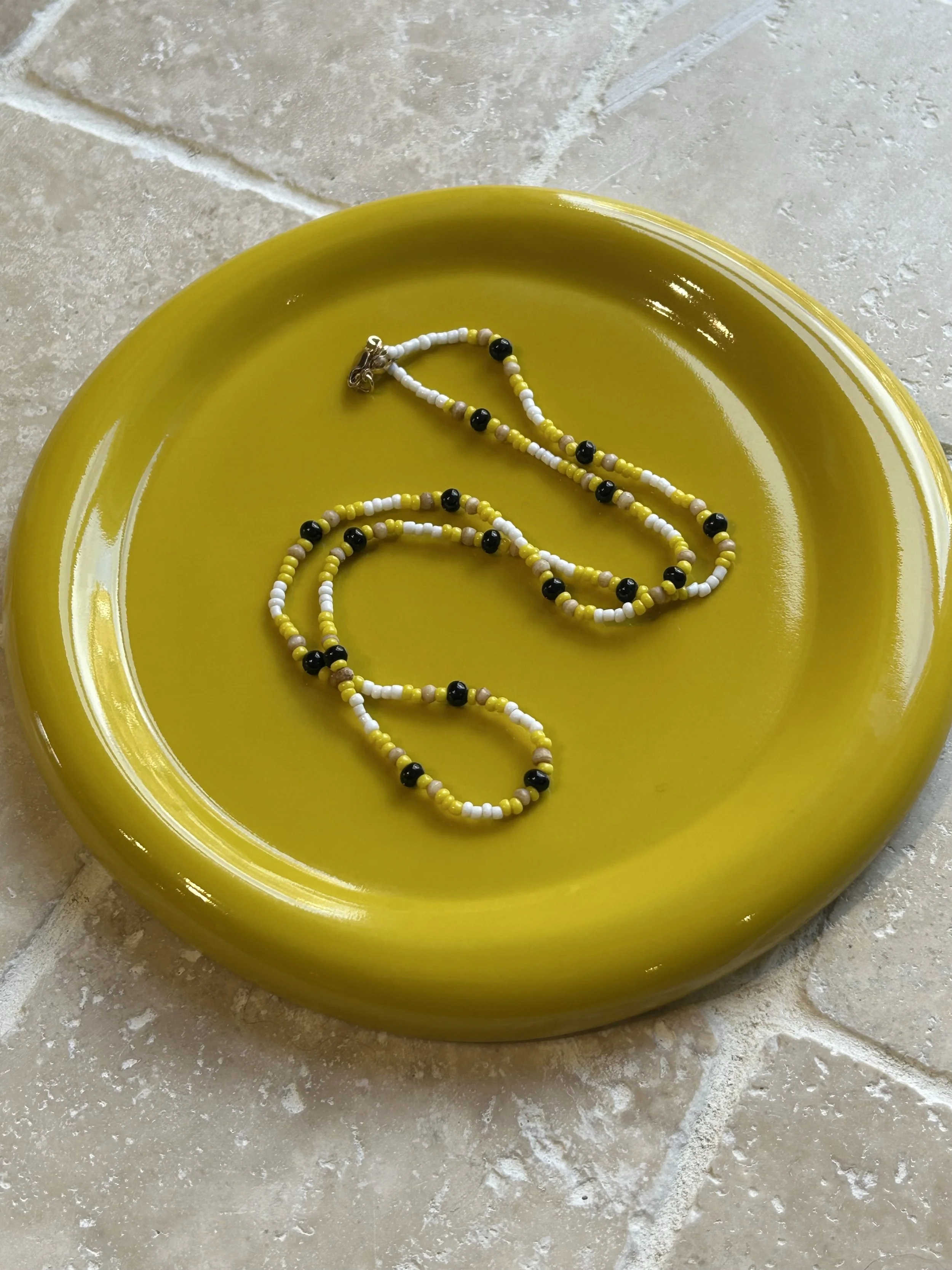 Vintage beaded necklace with black, white, yellow, and wooden beads lying on a yellow plate made by softedge.